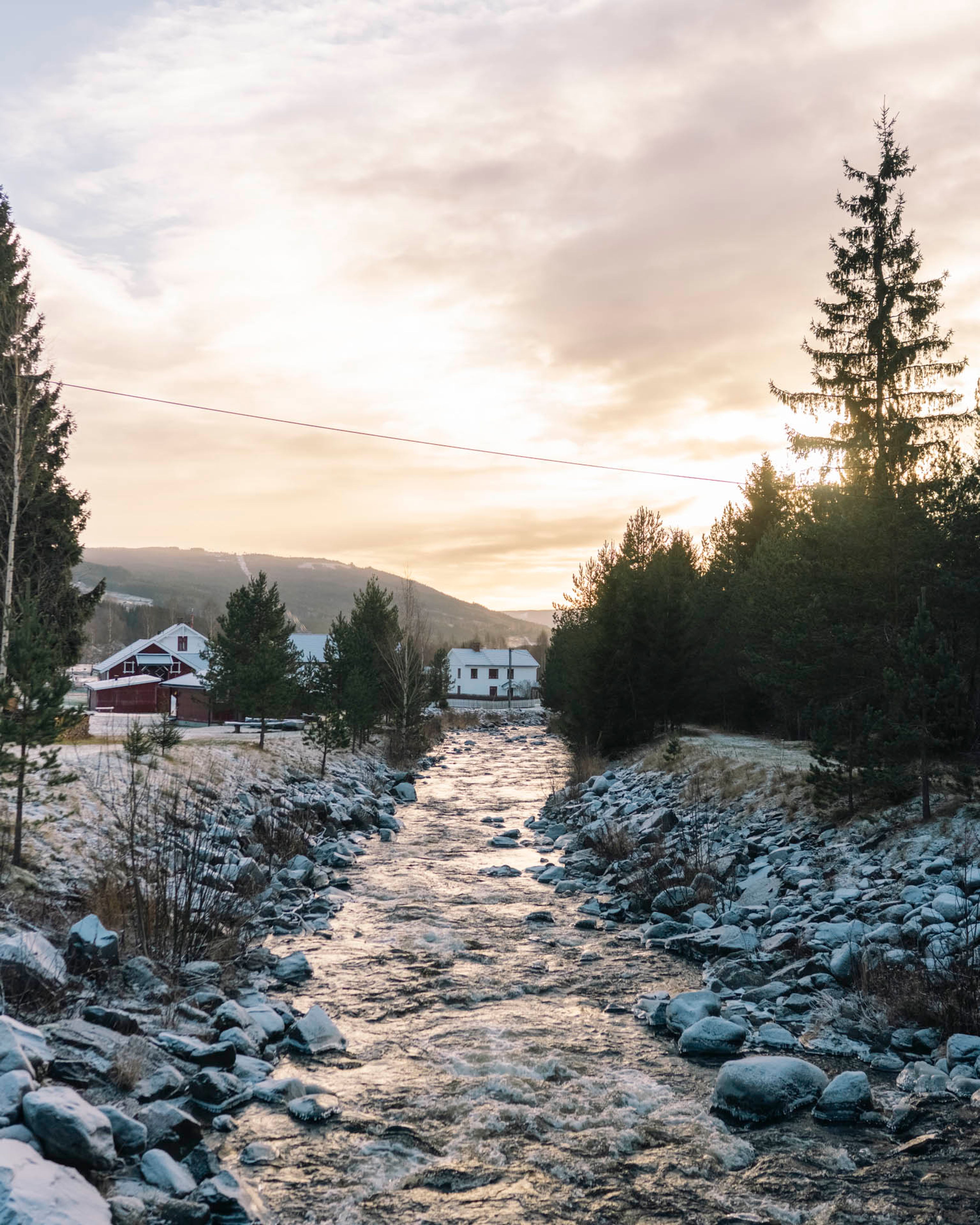 Bekk i fjellområde med snø langs breddene og vinterlige forhold rundt bebyggelse.