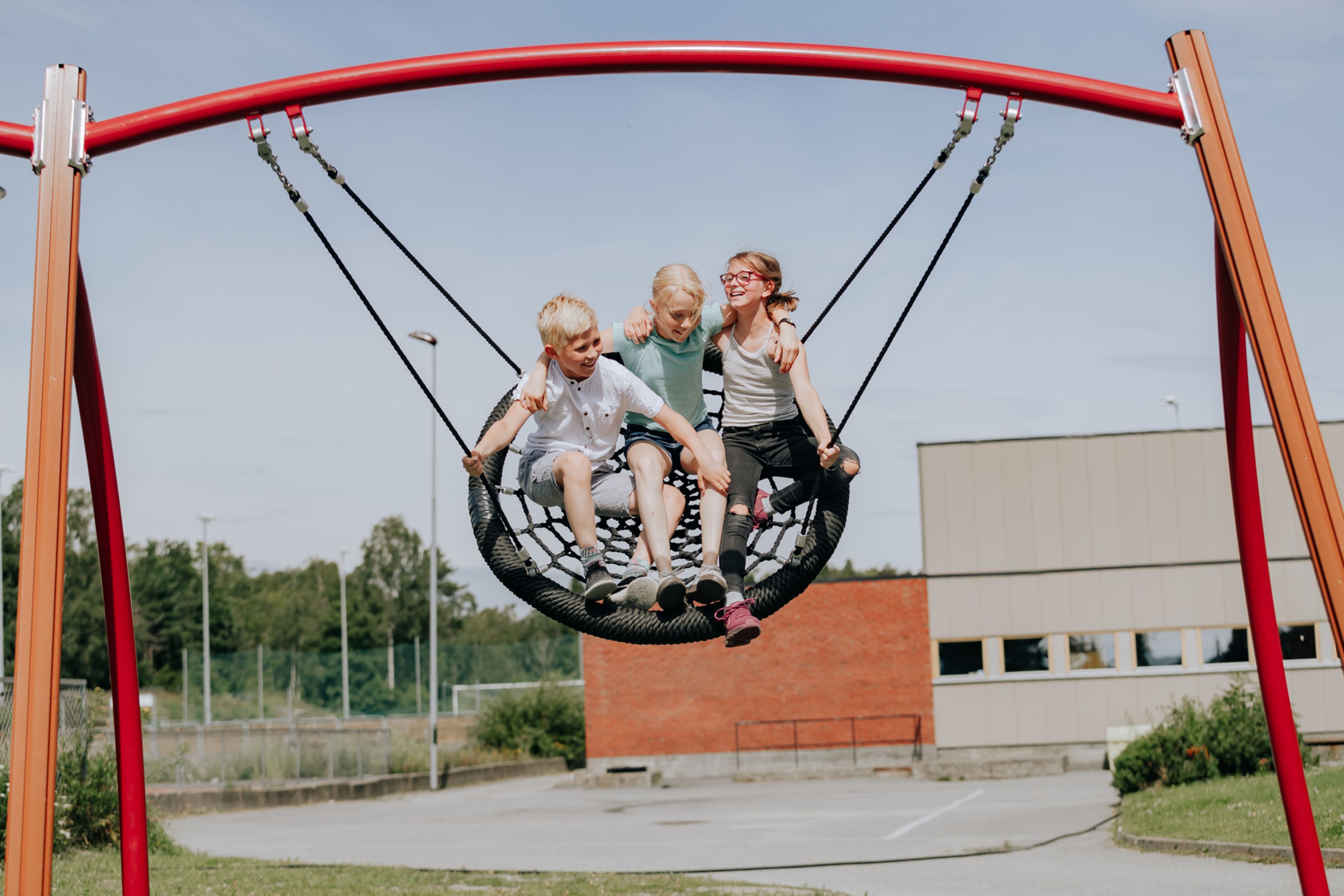 Tre barn bruker huska på lekeplassen.