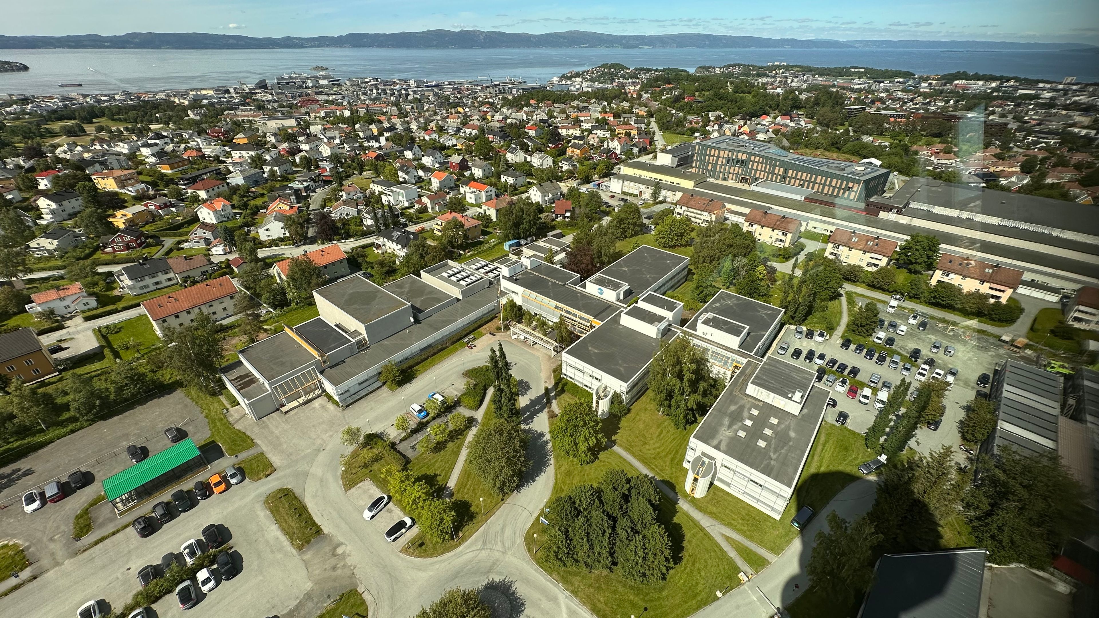 Oversiktsbilde over tomta på Tyholt, med hus og utsikt til vannet.