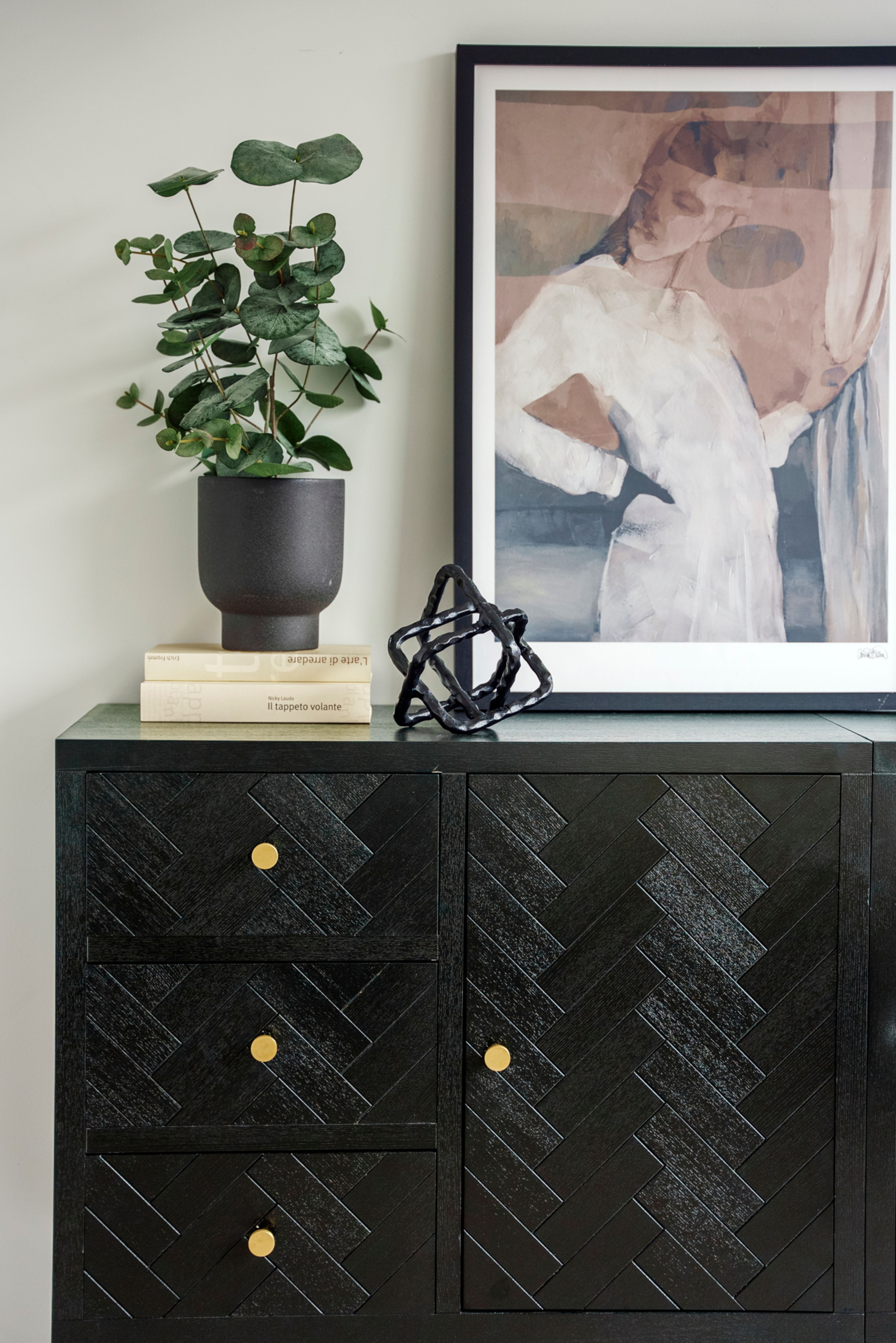 En sort skjenk med maleri, bøker og planter på toppen.