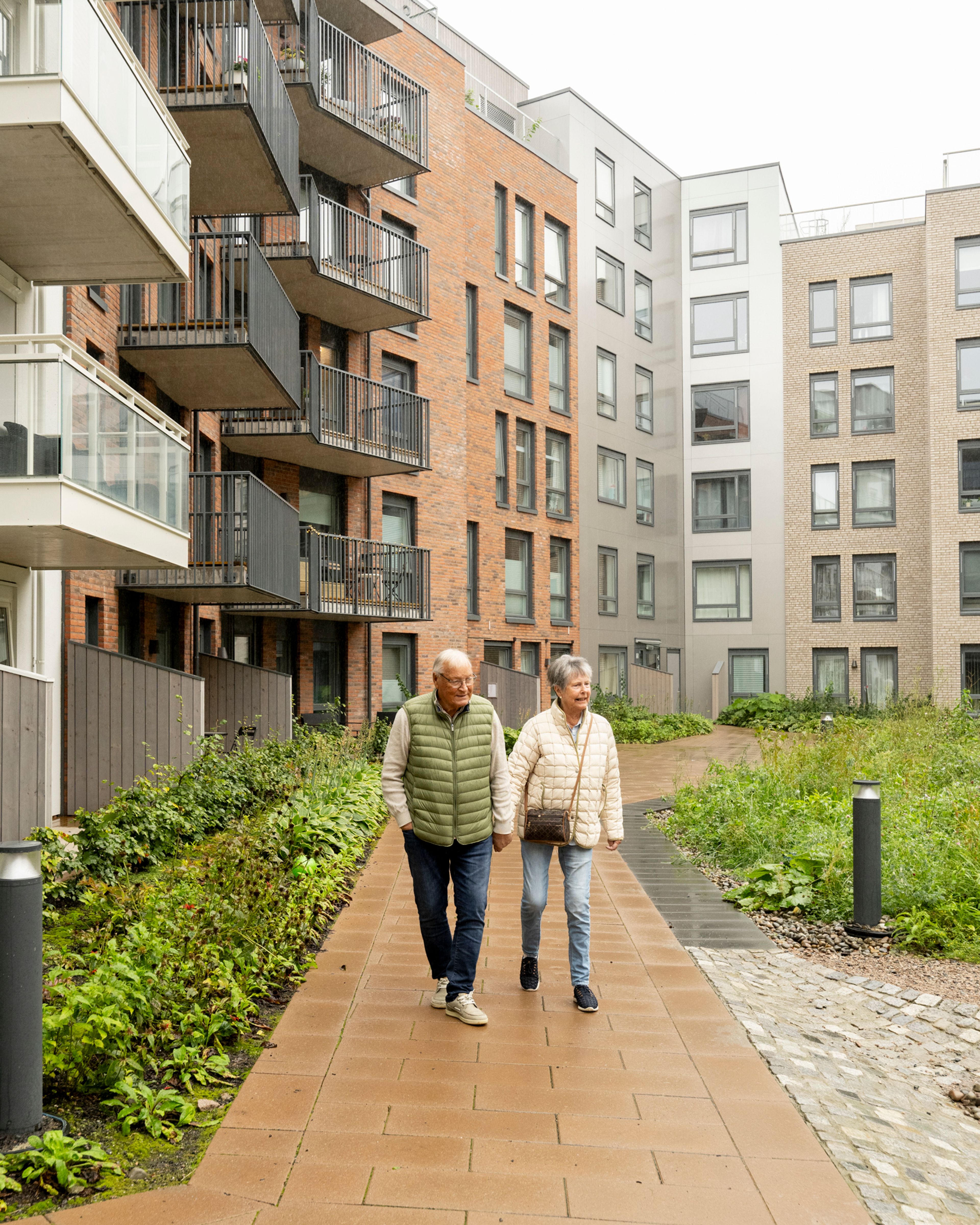 Foto av beboerne Clas og Lise som går gjennom uteområdene til nabolaget i Vollebekk Torgkvartal.