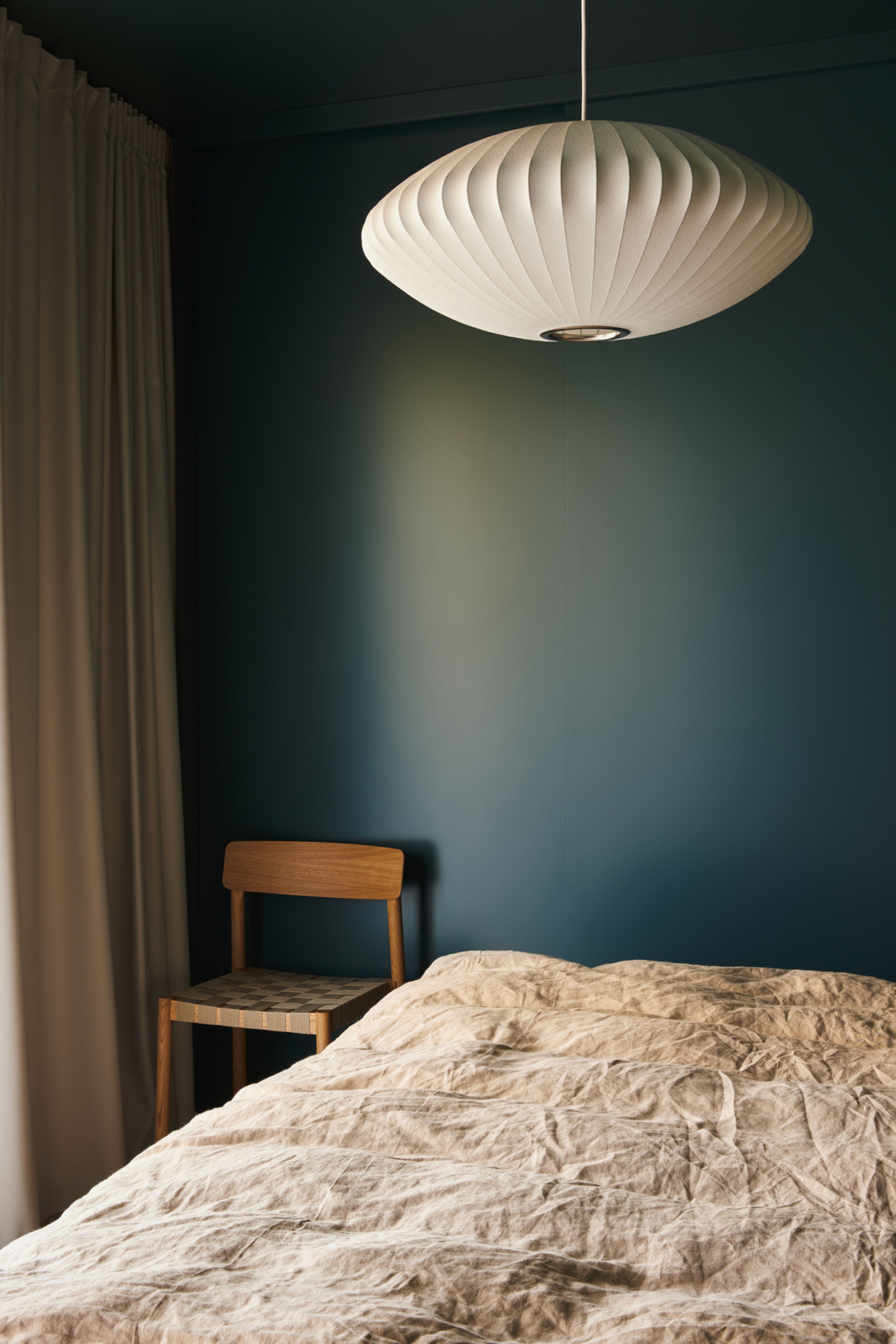 Mørkt blåmalt soverom med seng og hvit taklampe