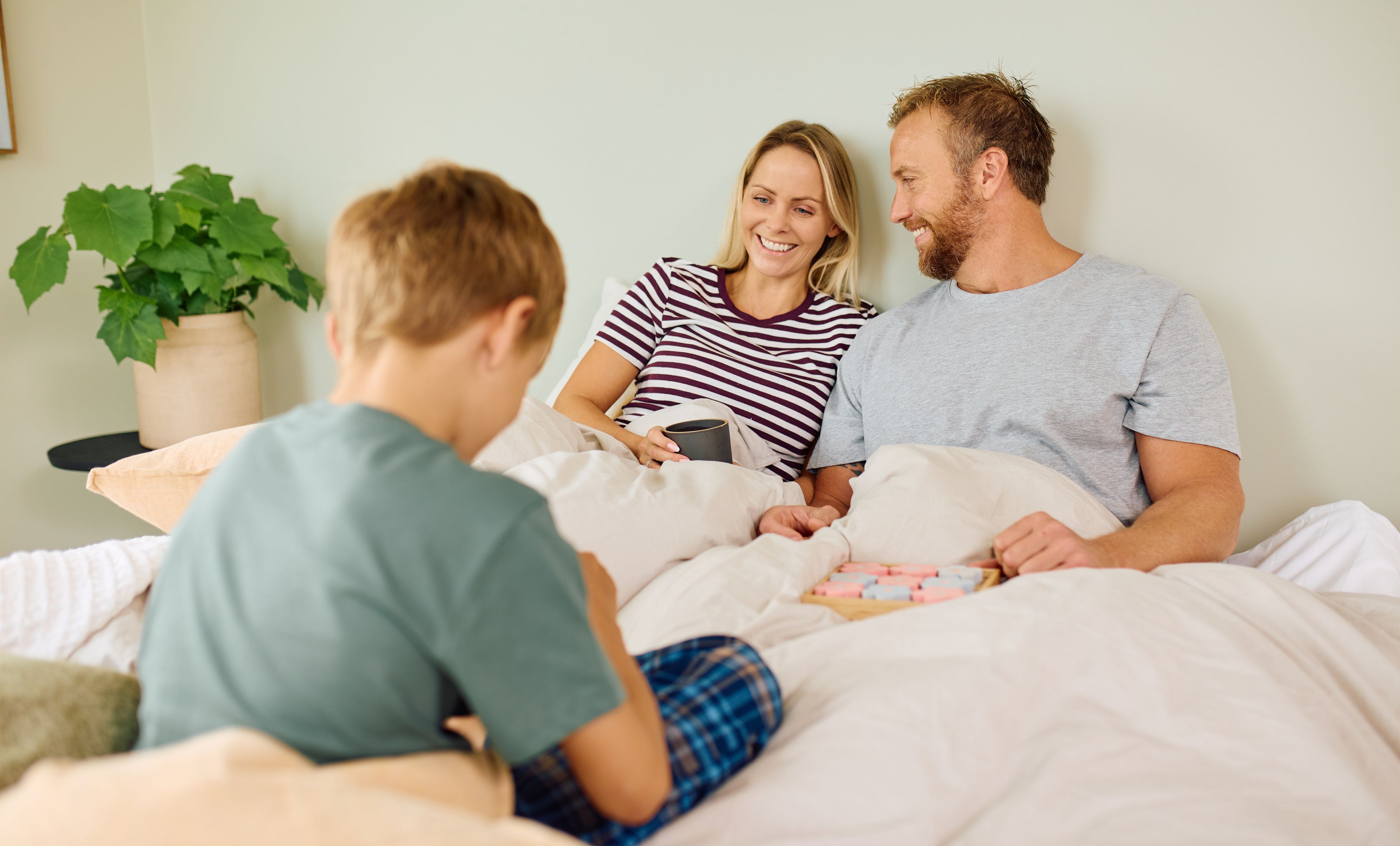 En mann og en dame er i lag med tre barn. De leker og mannen smiler bredt.