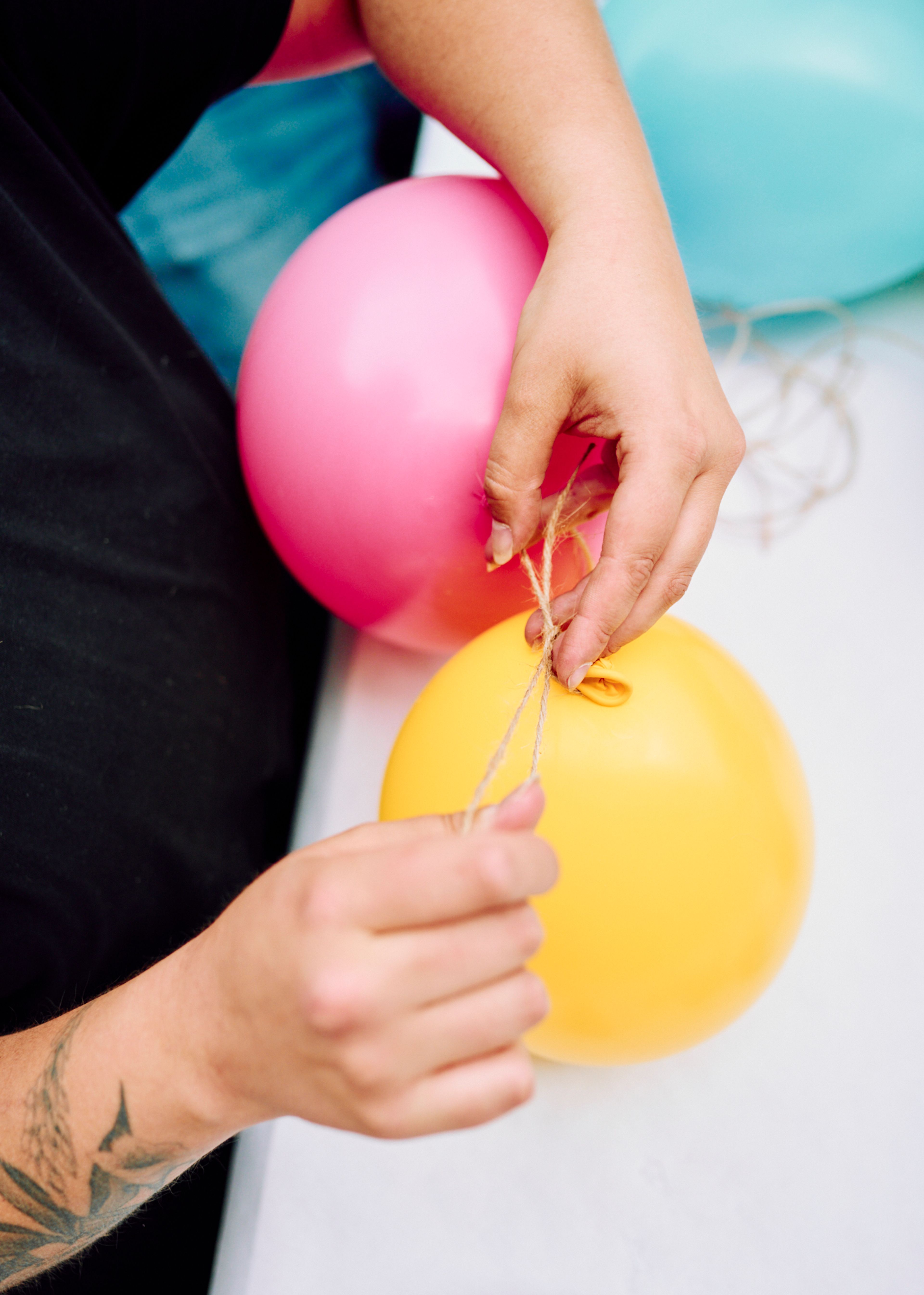 Hender som knyter sammen rosa og gule ballonger