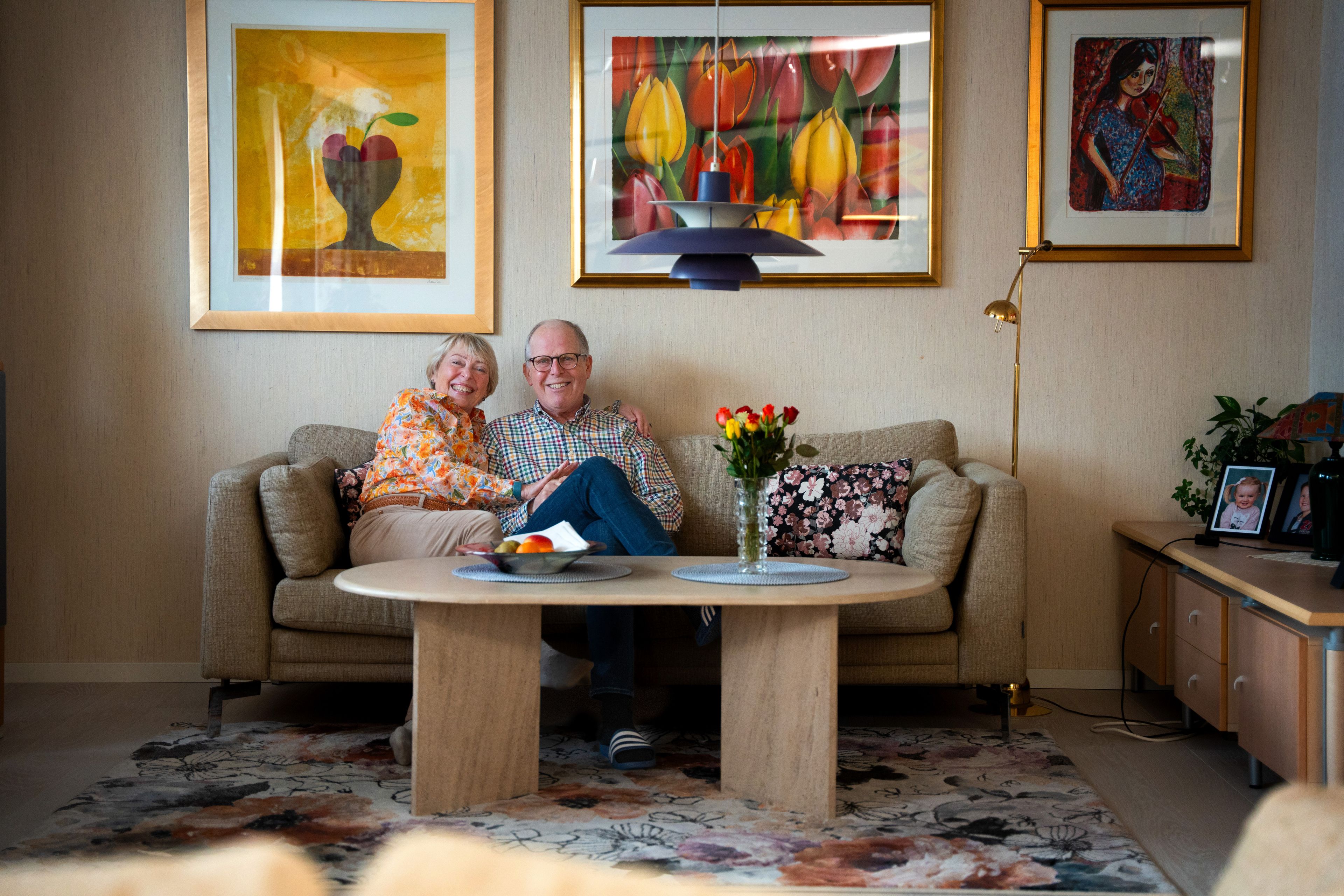 Smilende par sitter tett sammen i sofaen i en lys og fargerik stue med kunst på veggene.