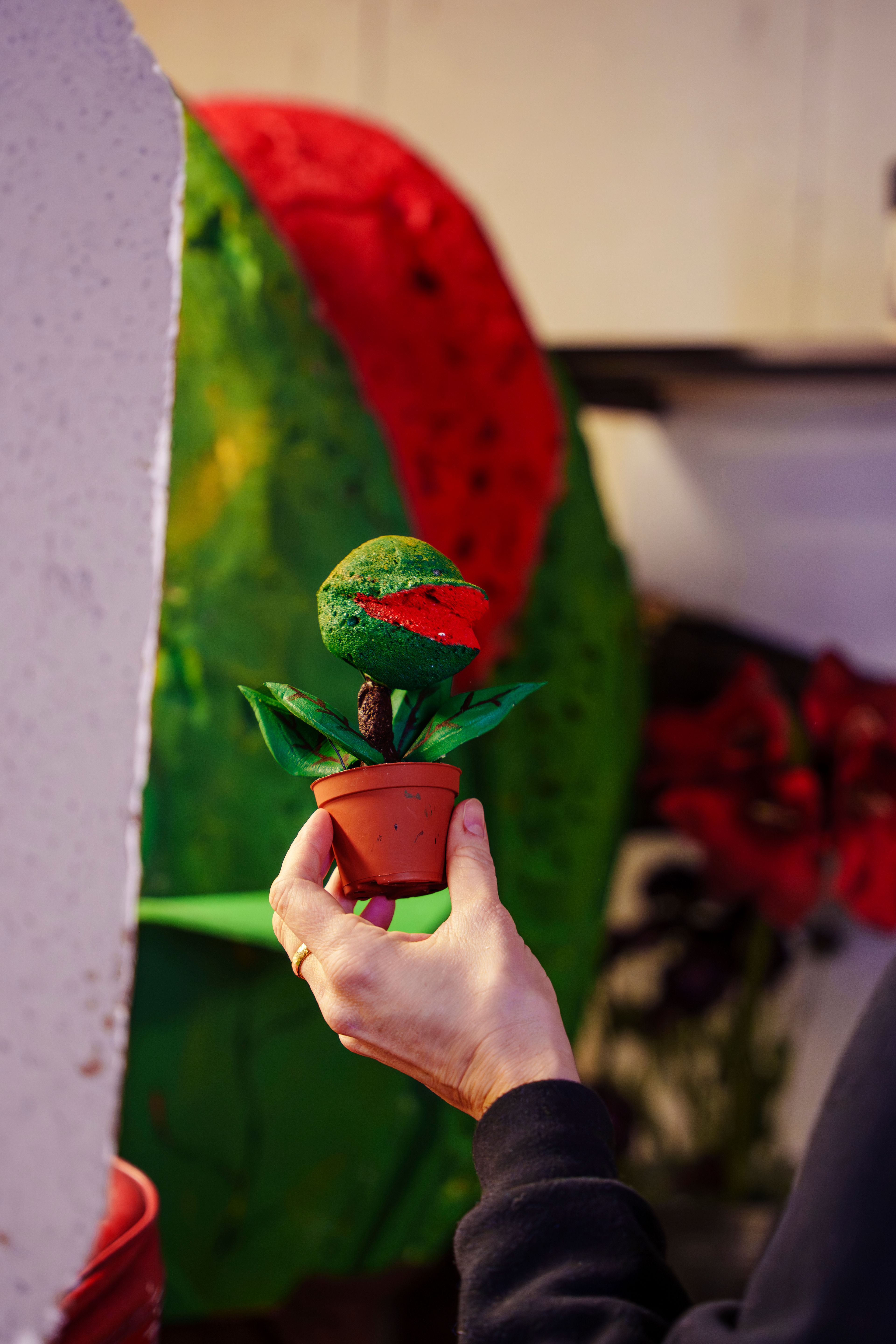 En hånd holder en liten håndlaget rekvisitt av en kjøttetende plante foran en større variant av samme motiv.