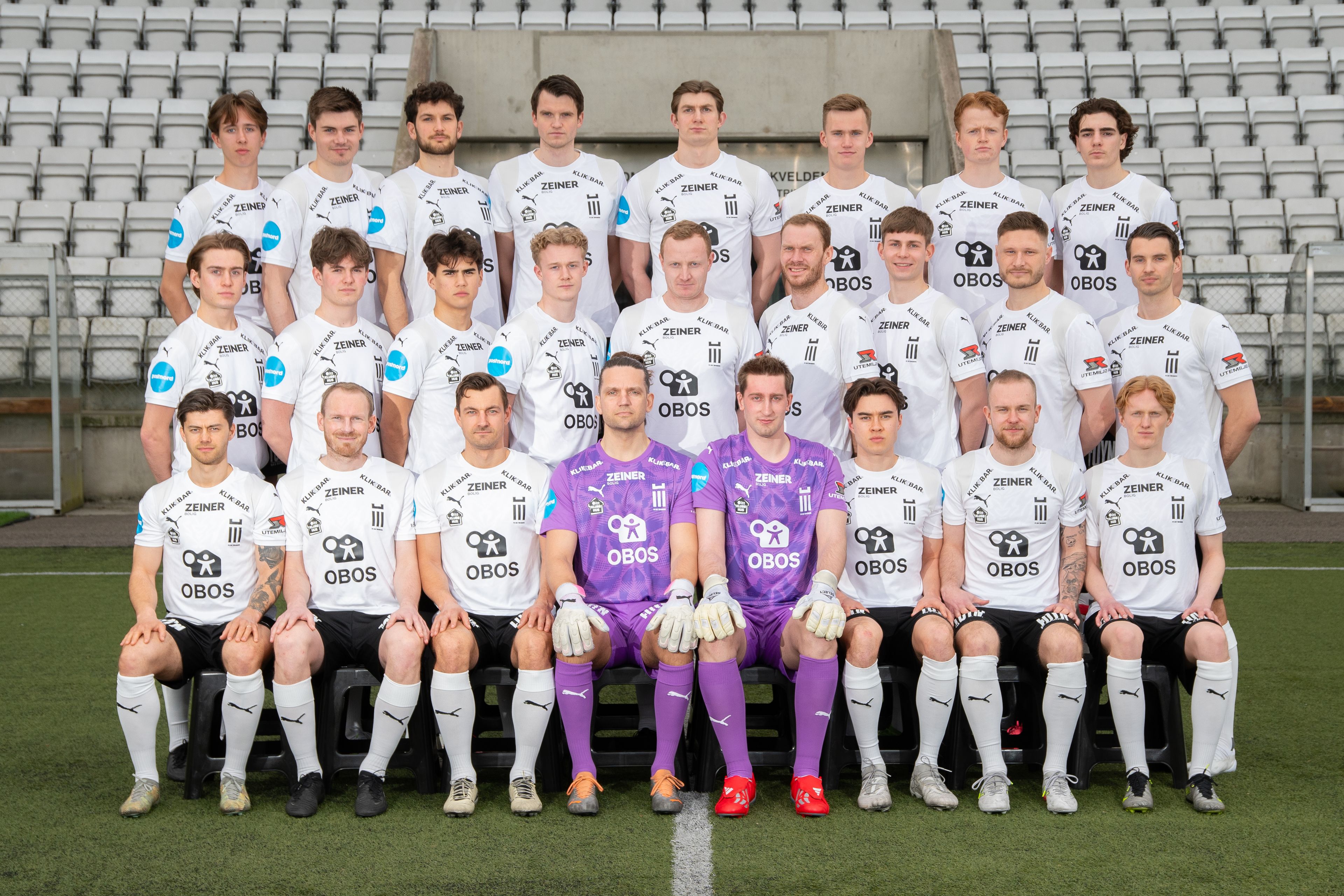 Oppstilt lagbilde med 25 mannlige fotballspillere som ser seriøst mot kameraet.