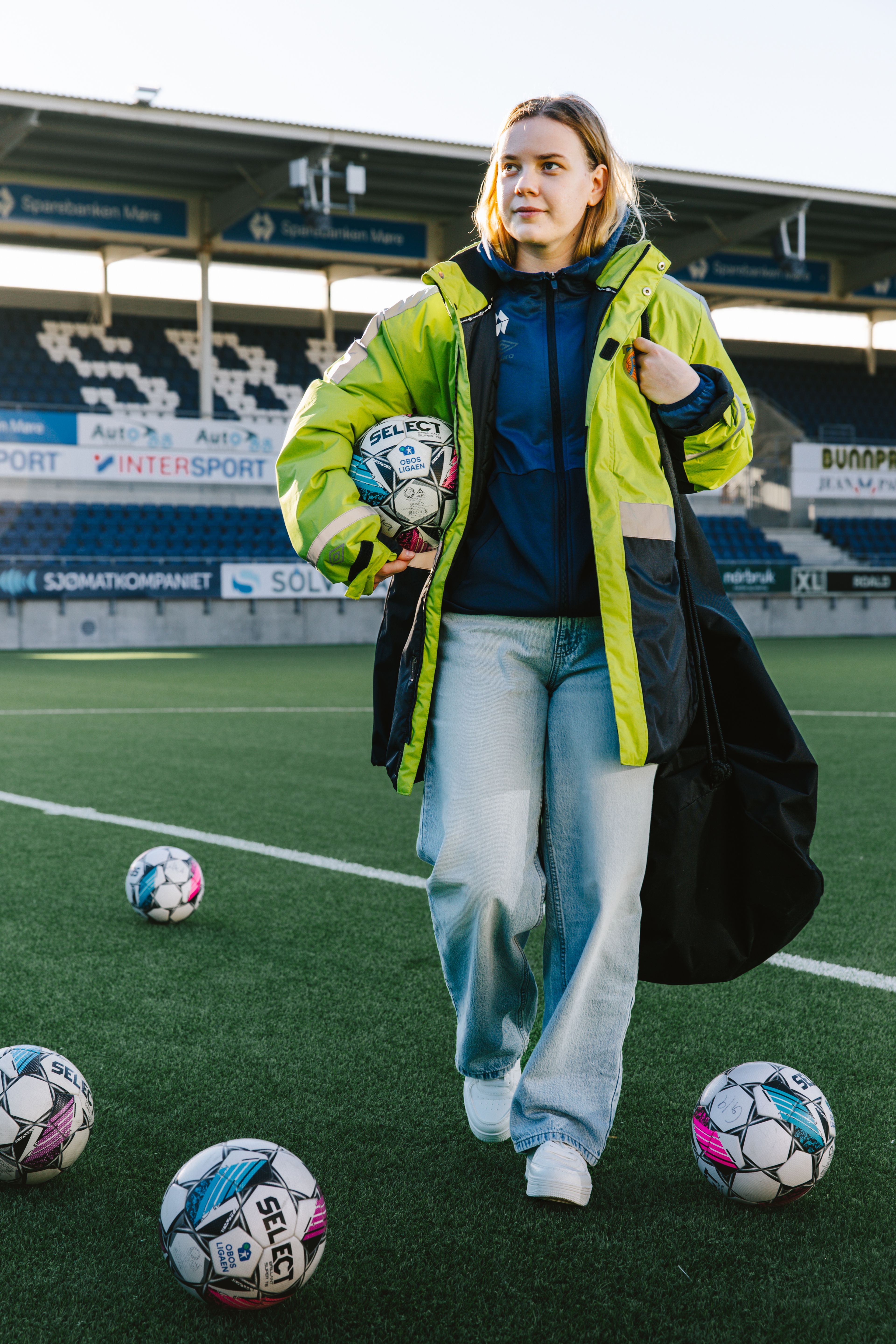 Kristina krysser kunstgresset med en fotball i hånden mens flere baller ligger spredt rundt på banen før oppvarming.