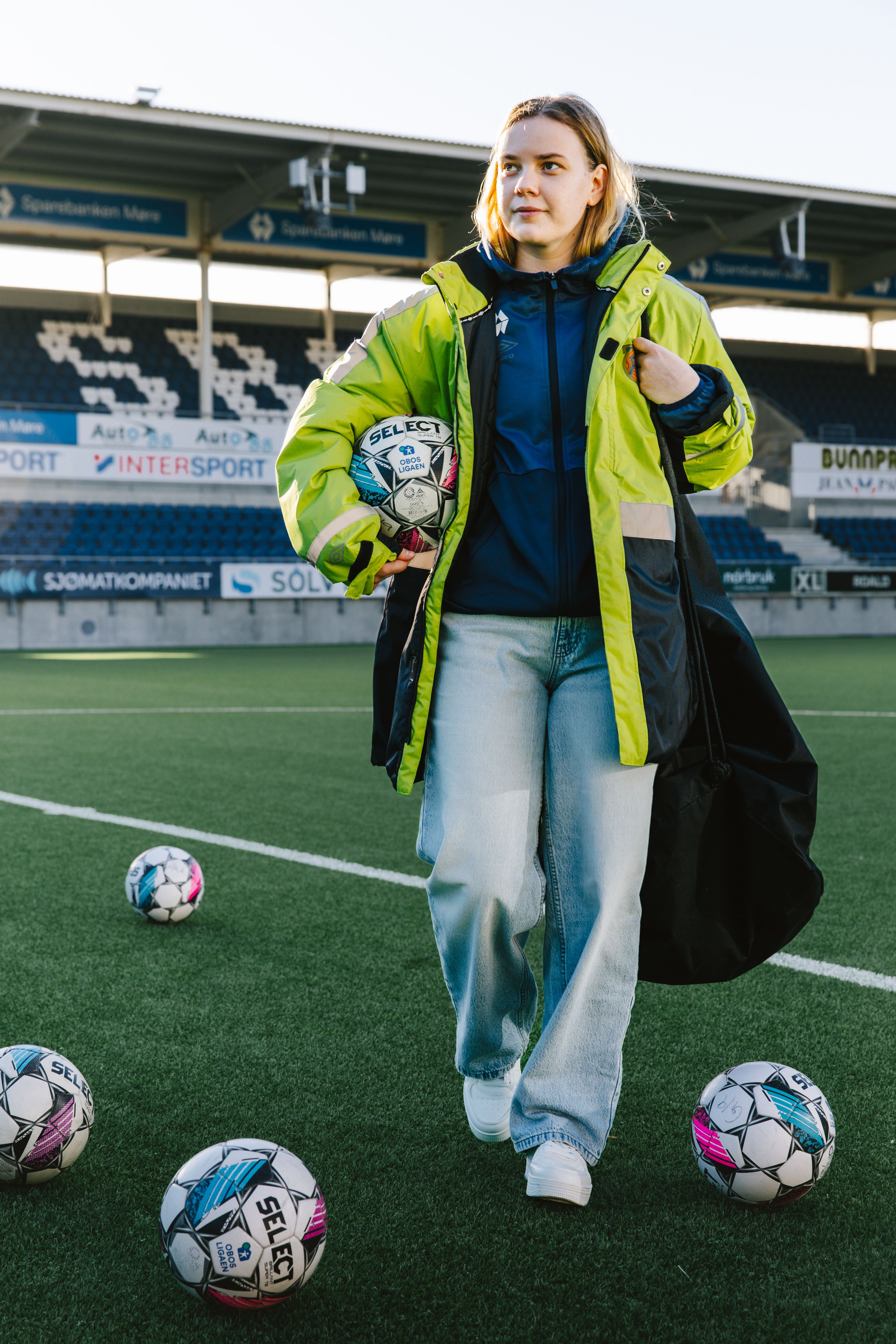 Kristina krysser kunstgresset med en fotball i hånden mens flere baller ligger spredt rundt på banen før oppvarming.