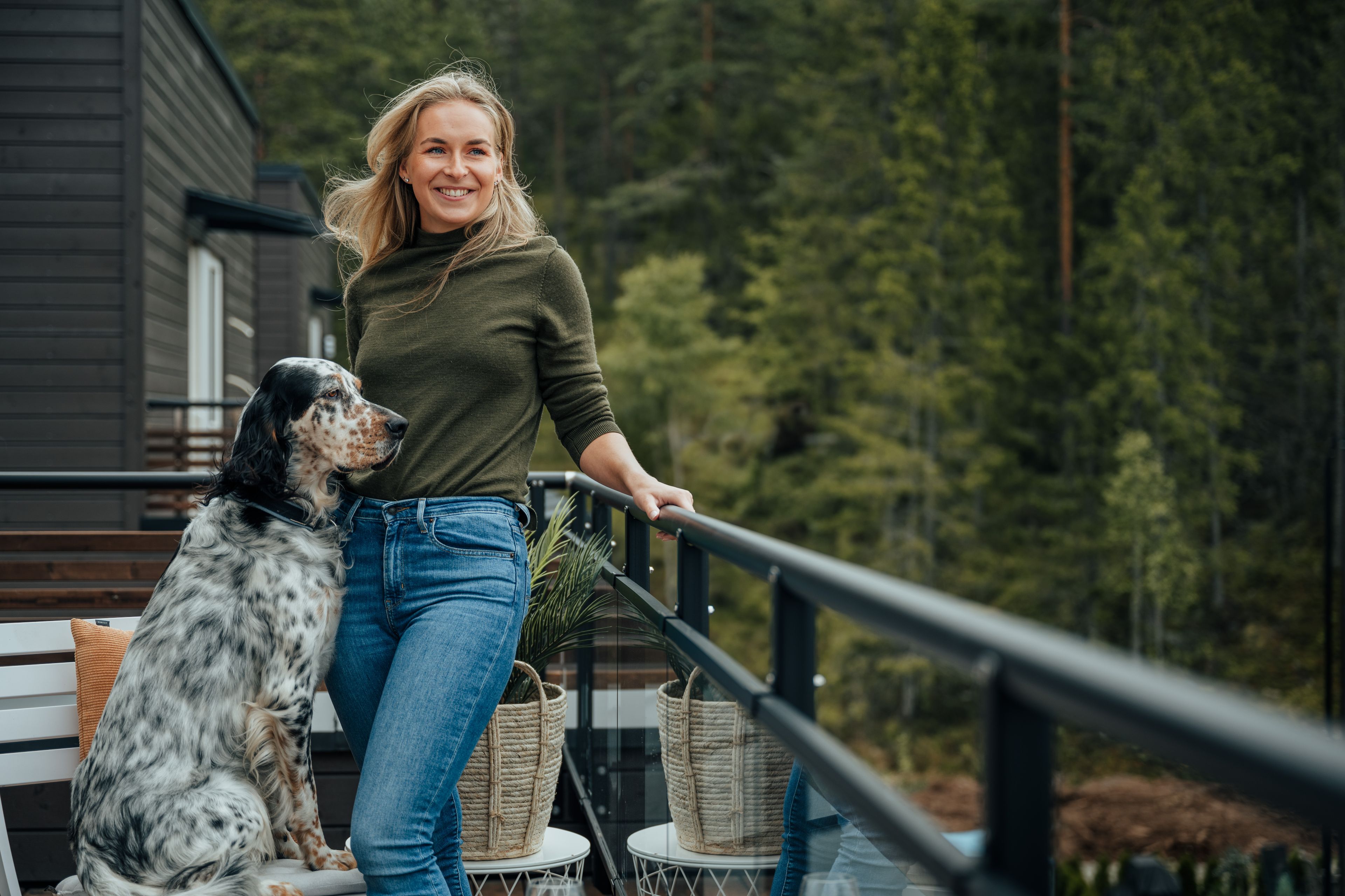 Ei dame står på en balkong med hunden sin ved siden av seg.