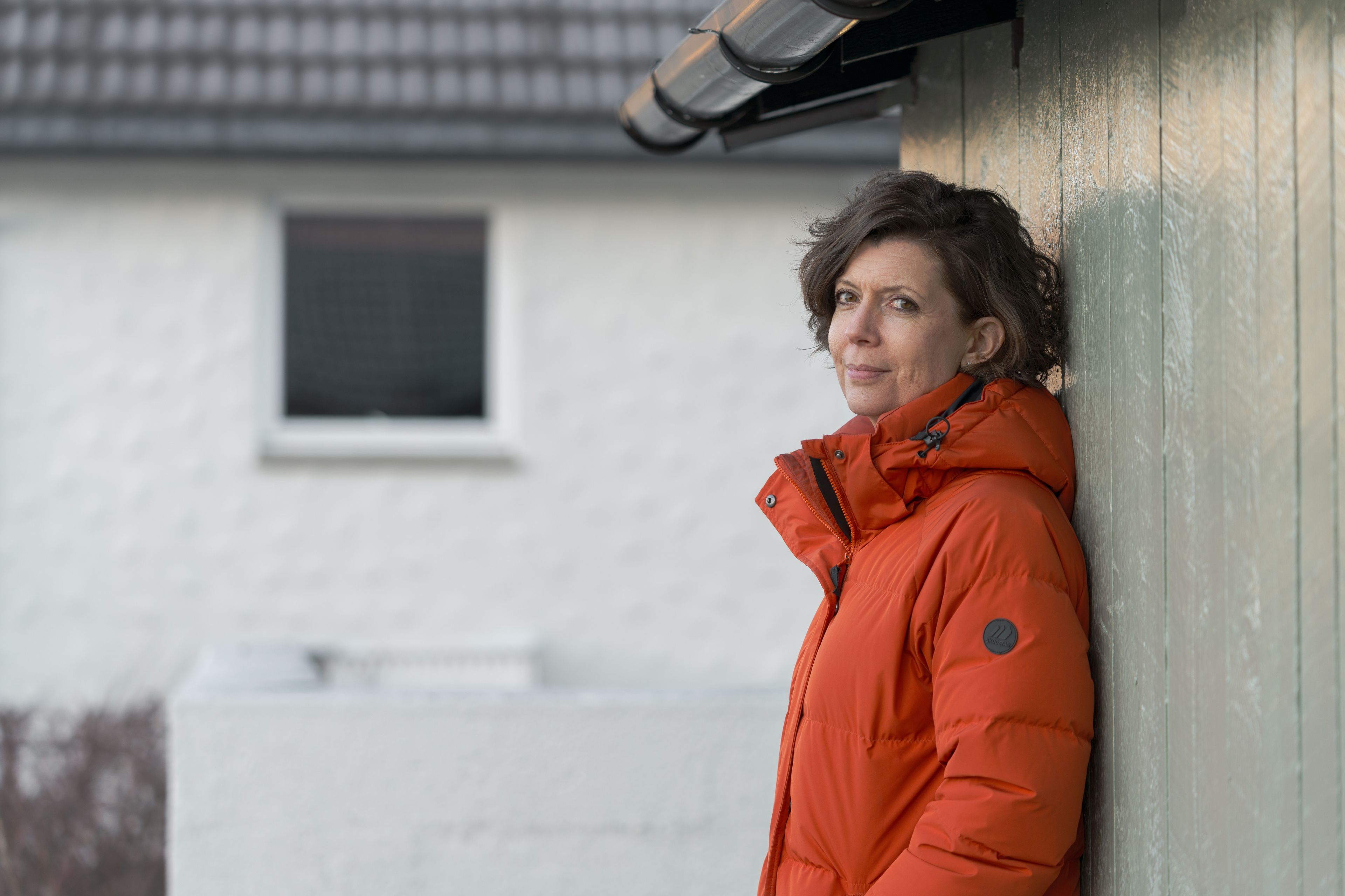 Kvinne står inntil husveggen og ser i kamera