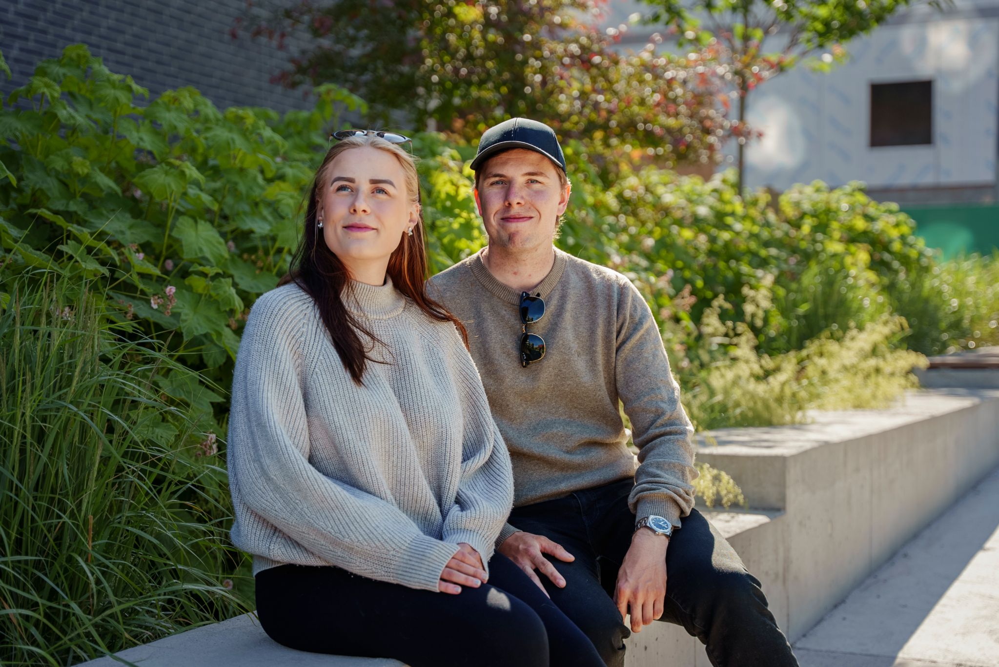 Svehagen og Jensen sitter på en sementbenk mot et bakteppe av grønne busker.