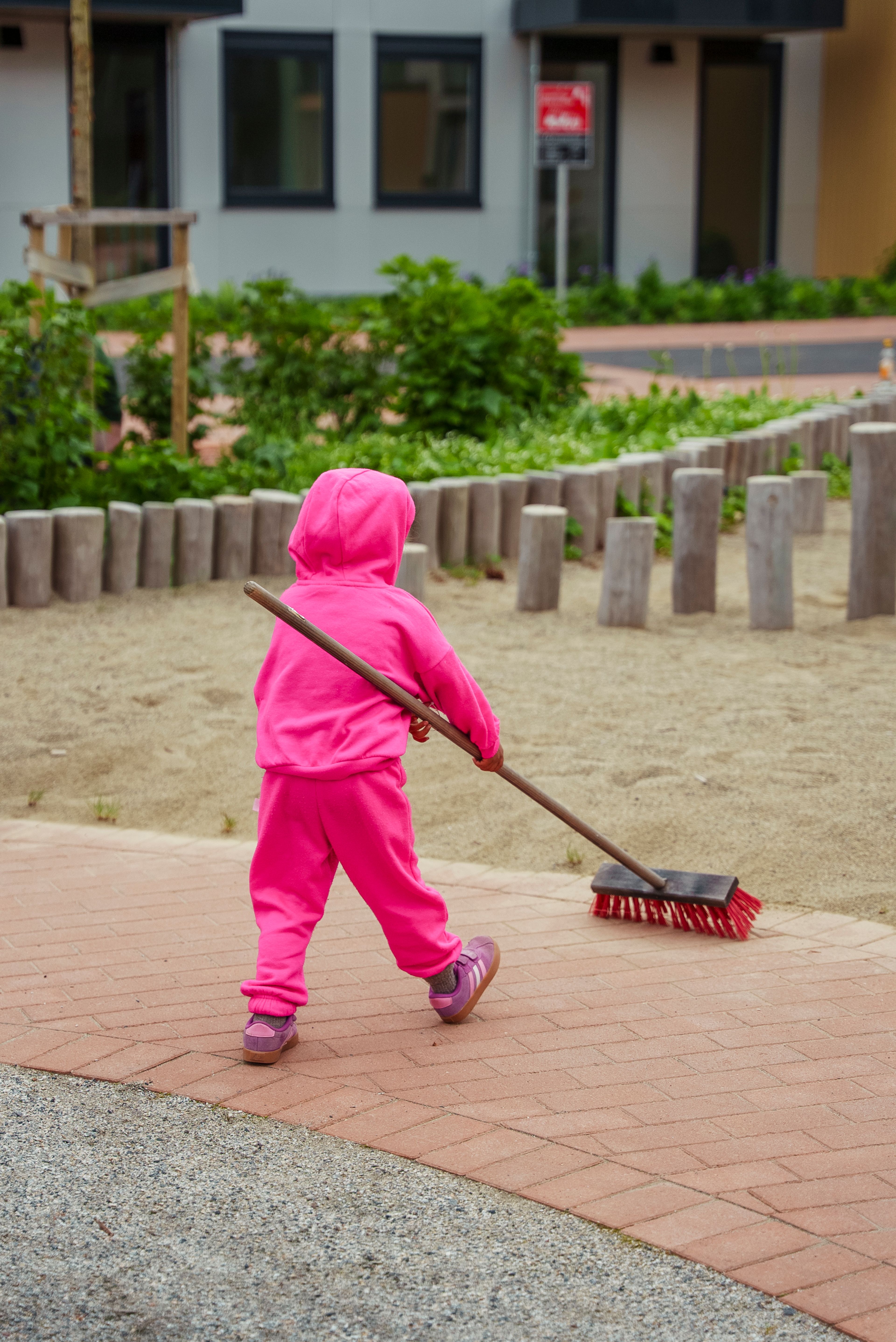 En unge i rosa genser og bukse koster sand