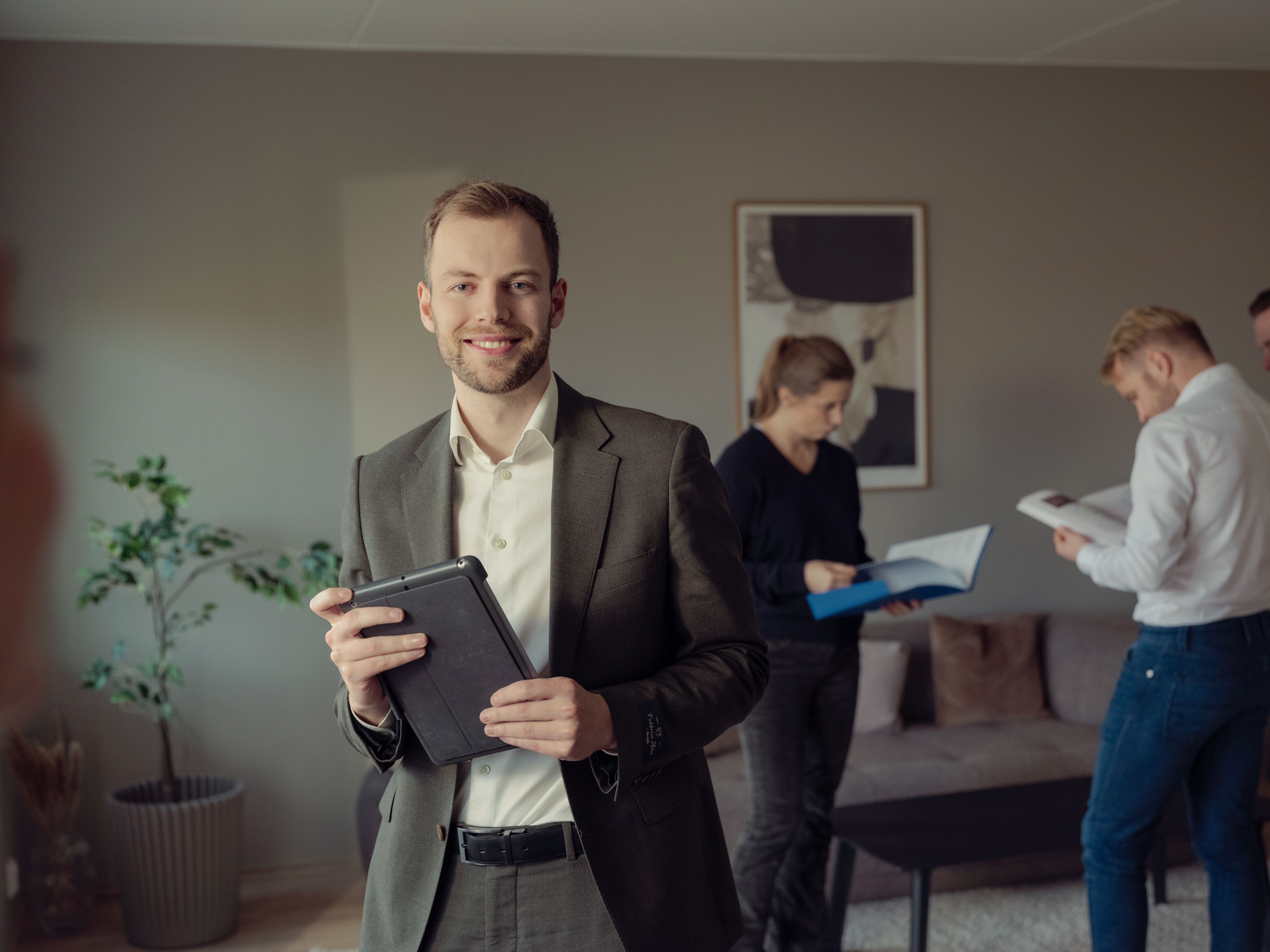 Megler på visning med en ipad i hånden med boligkjøpere i bakgrunnen.
