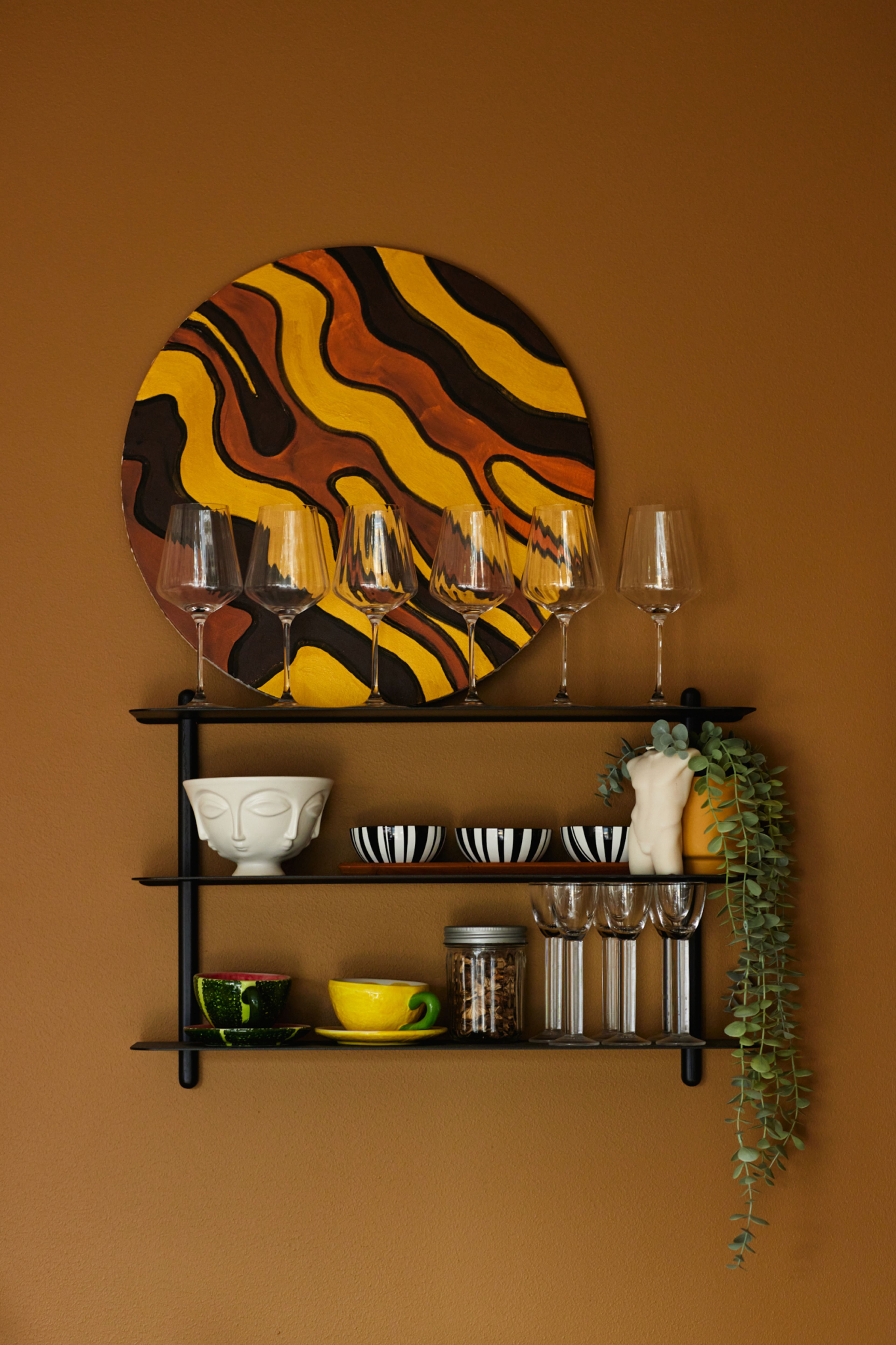 En hylle med vinglass, skåler og planter.