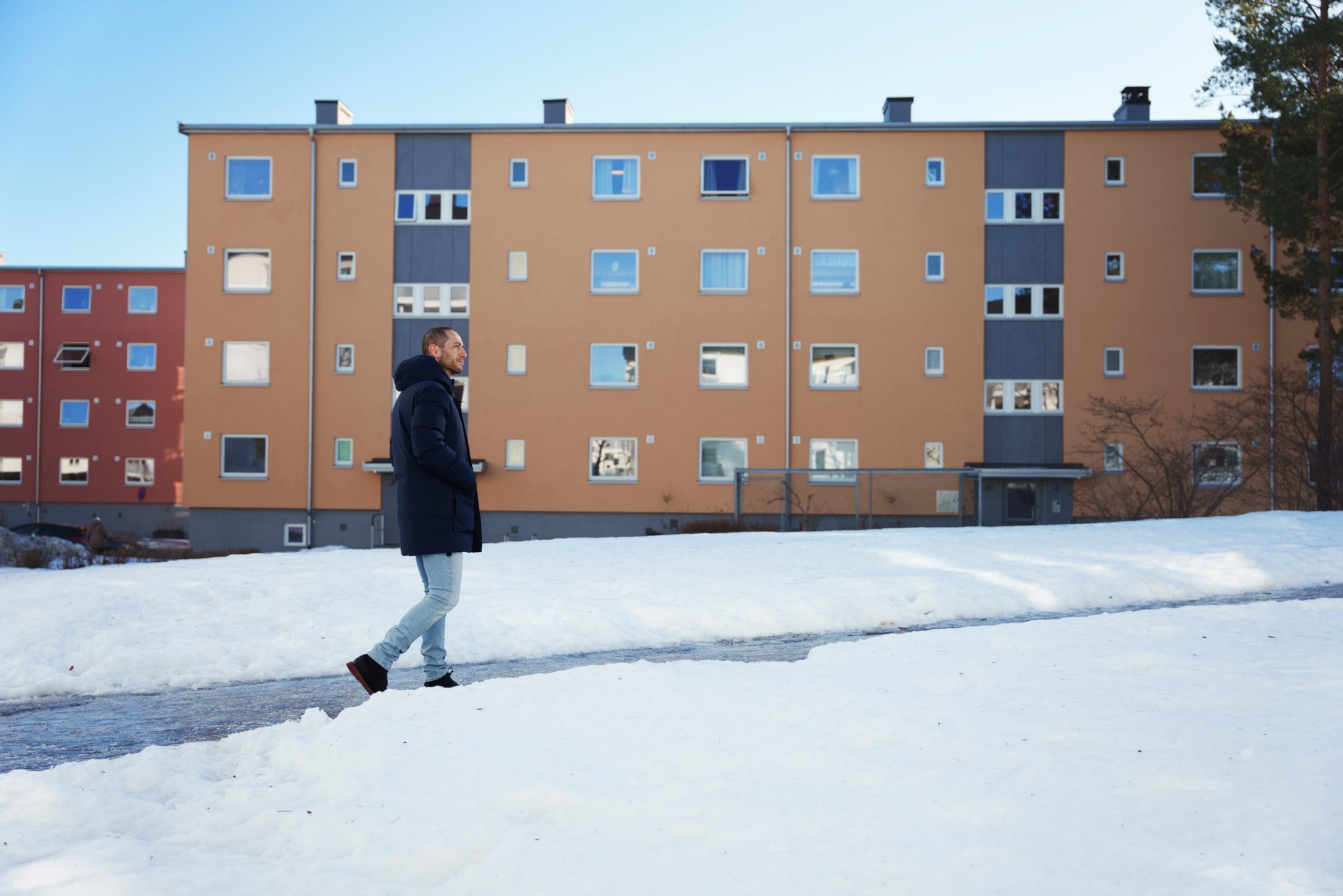 En mann går utenfor blokkene på Manglerud. Han har på seg en mørk jakke.