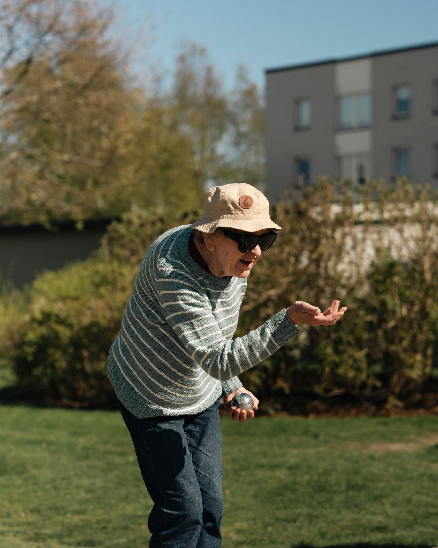 Person spiller petanque på gresset i et boligområde og gjør seg klar til å kaste en kule.