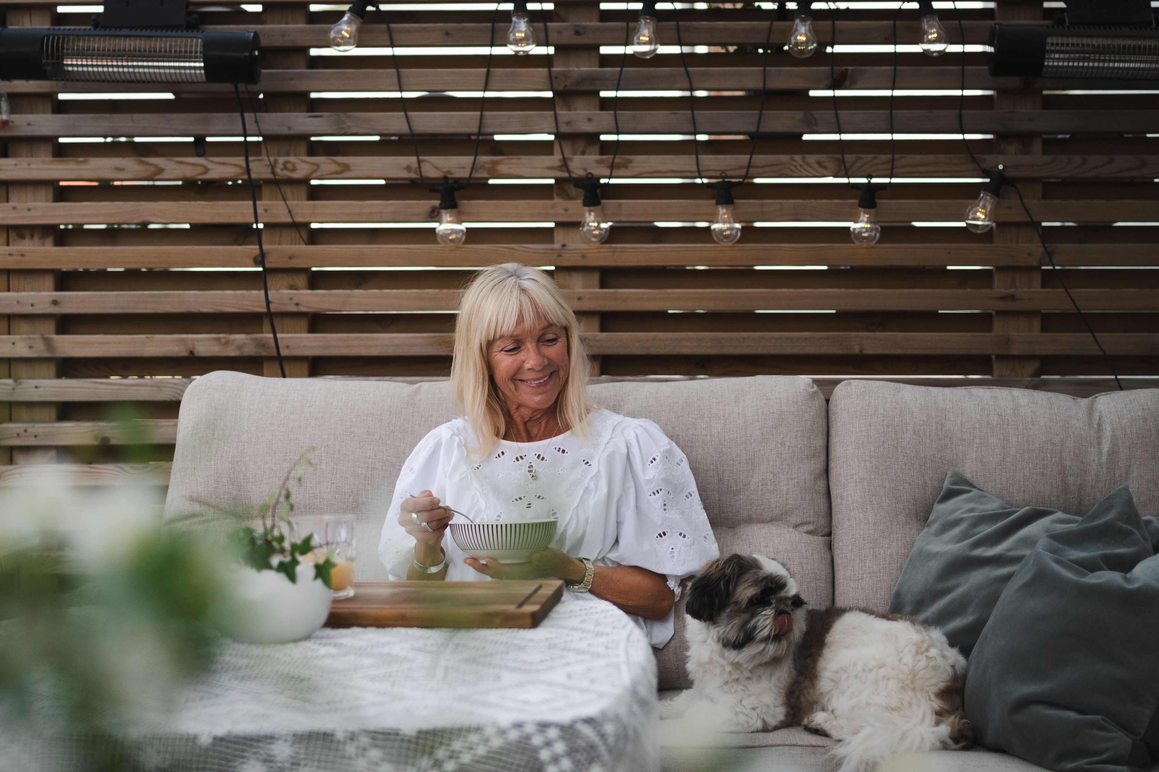 Foto på en kvinna och hund som sitter i en soffa på altanen, med skärmvägg bakom ryggen