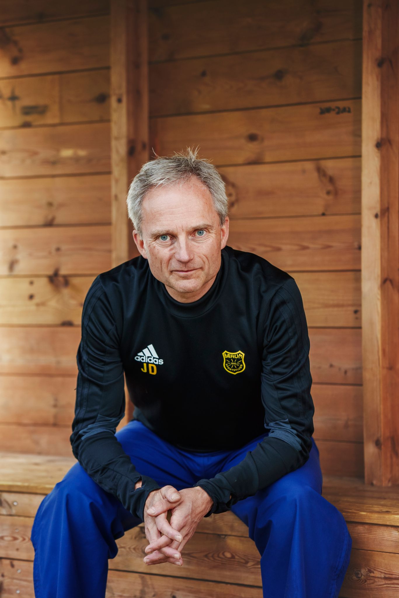 Jostein Djupvik sitter med hendene foldet og lener seg fram på trenerbenken av furu.