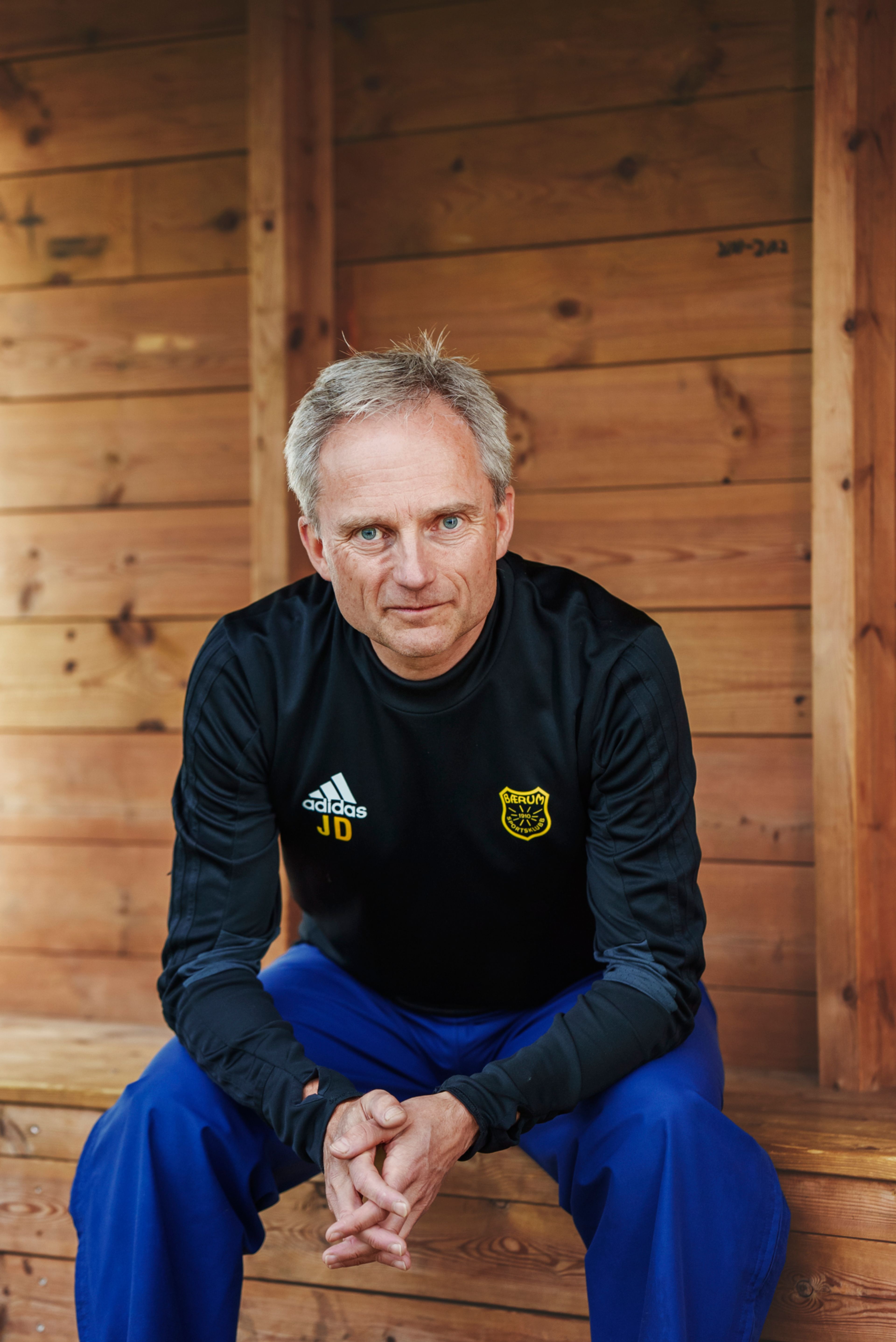 Jostein Djupvik sitter med hendene foldet og lener seg fram på trenerbenken av furu.