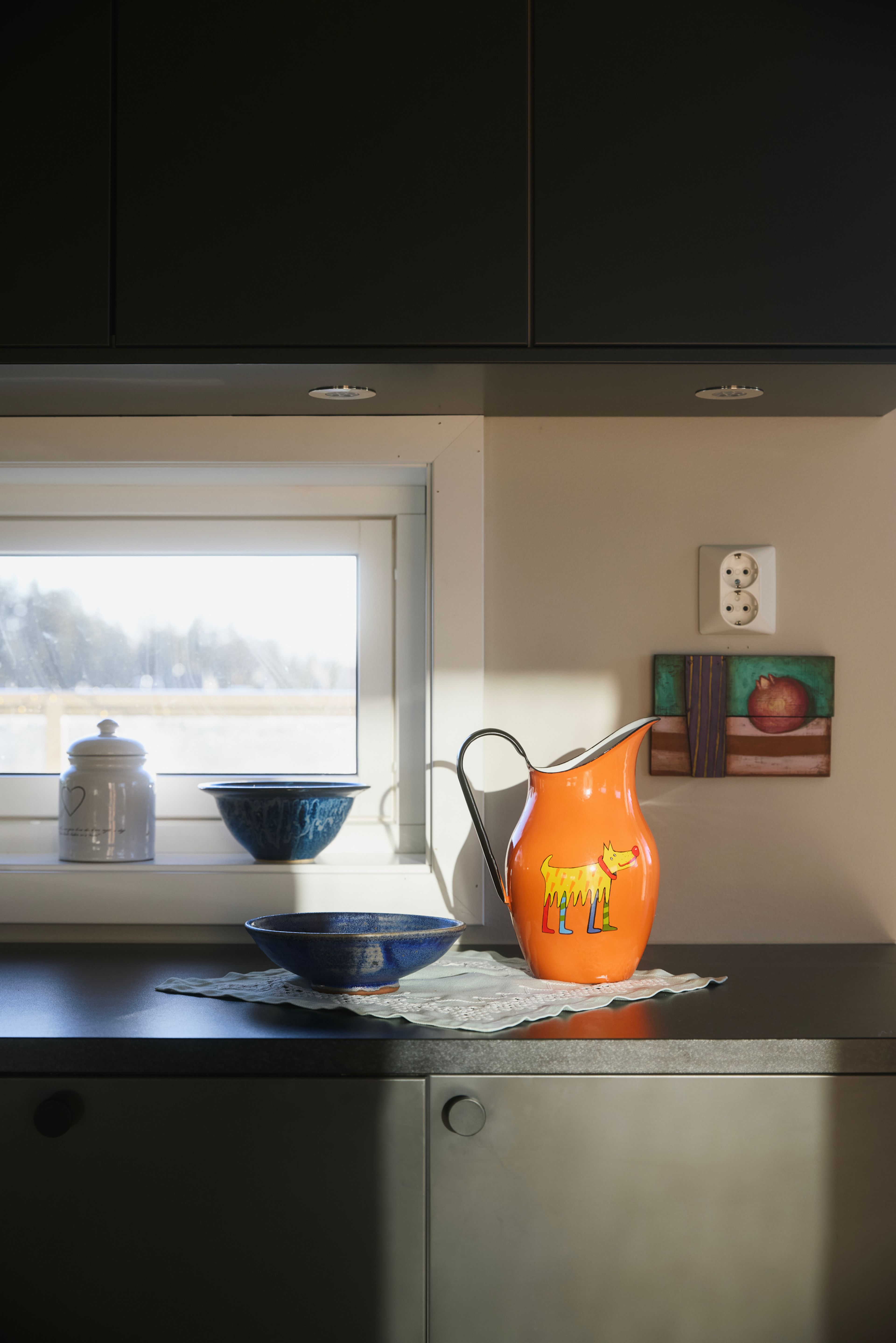Nærbilde av kjøkkenet som viser de mørke skapene, med en oransje vannkaraffel på benken