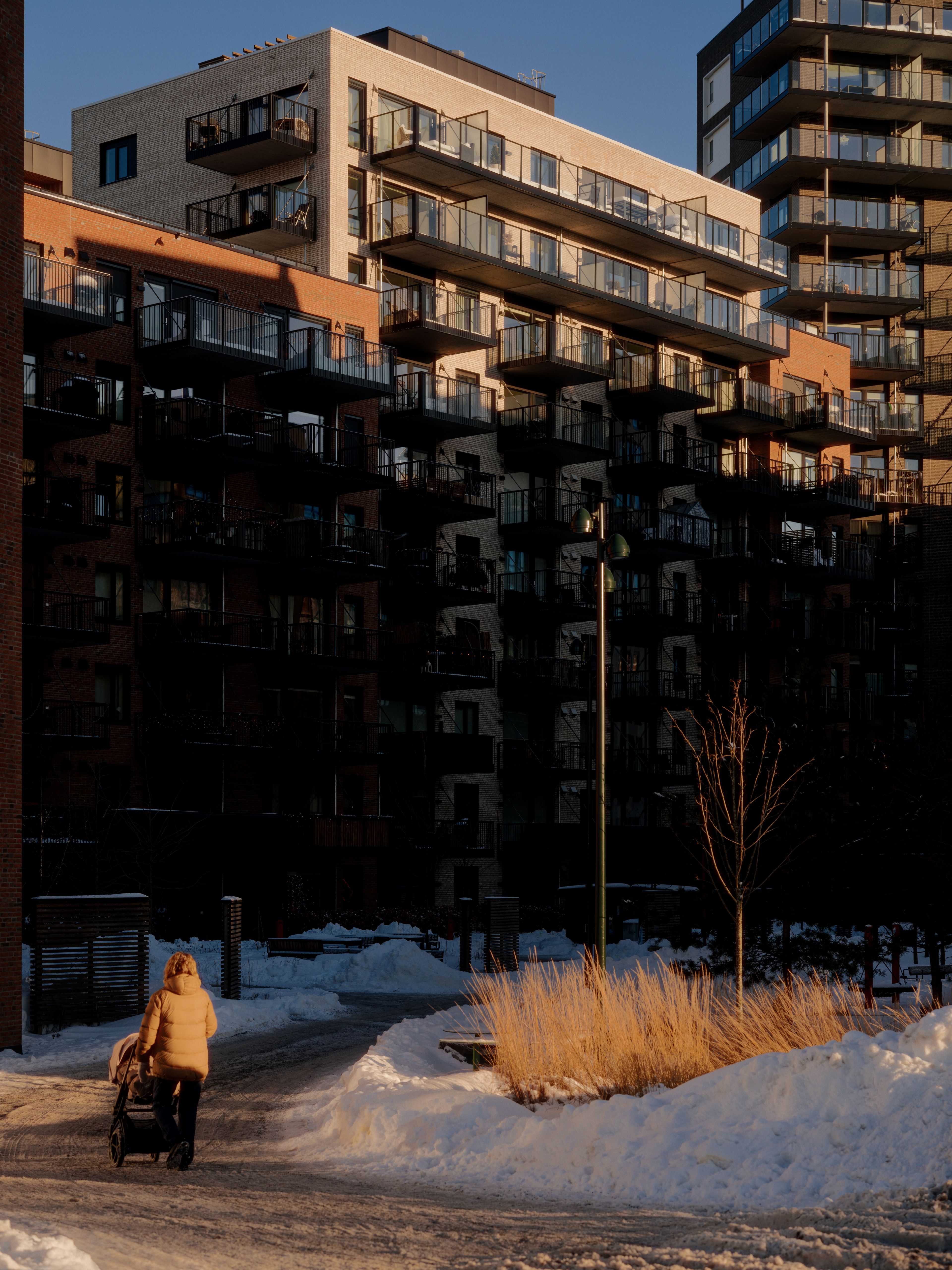 Dame som går med barnevogn på en snødekt gangvei foran boligblokker på Ulven