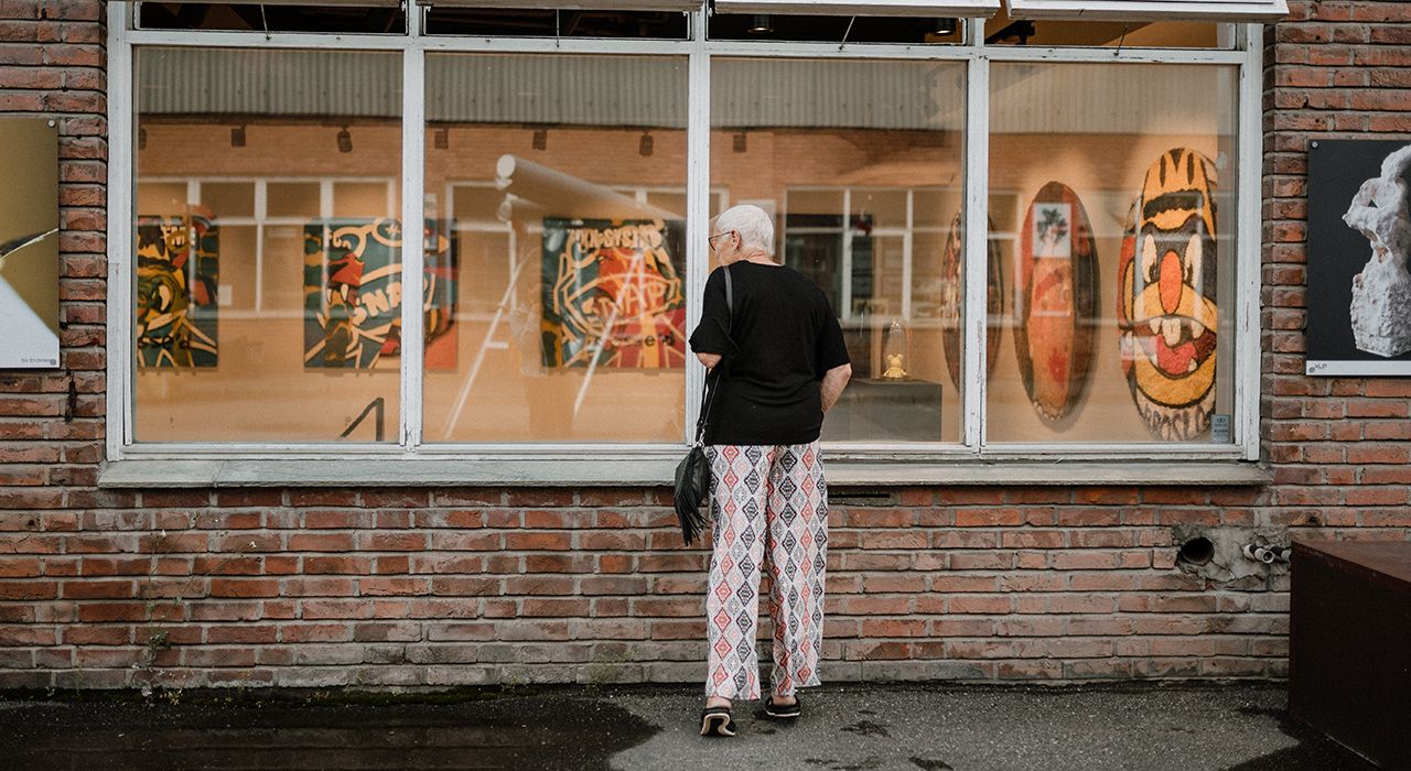 Eldre kvinne som titter inn i vinduet til et kunstgalleri på dagtid.