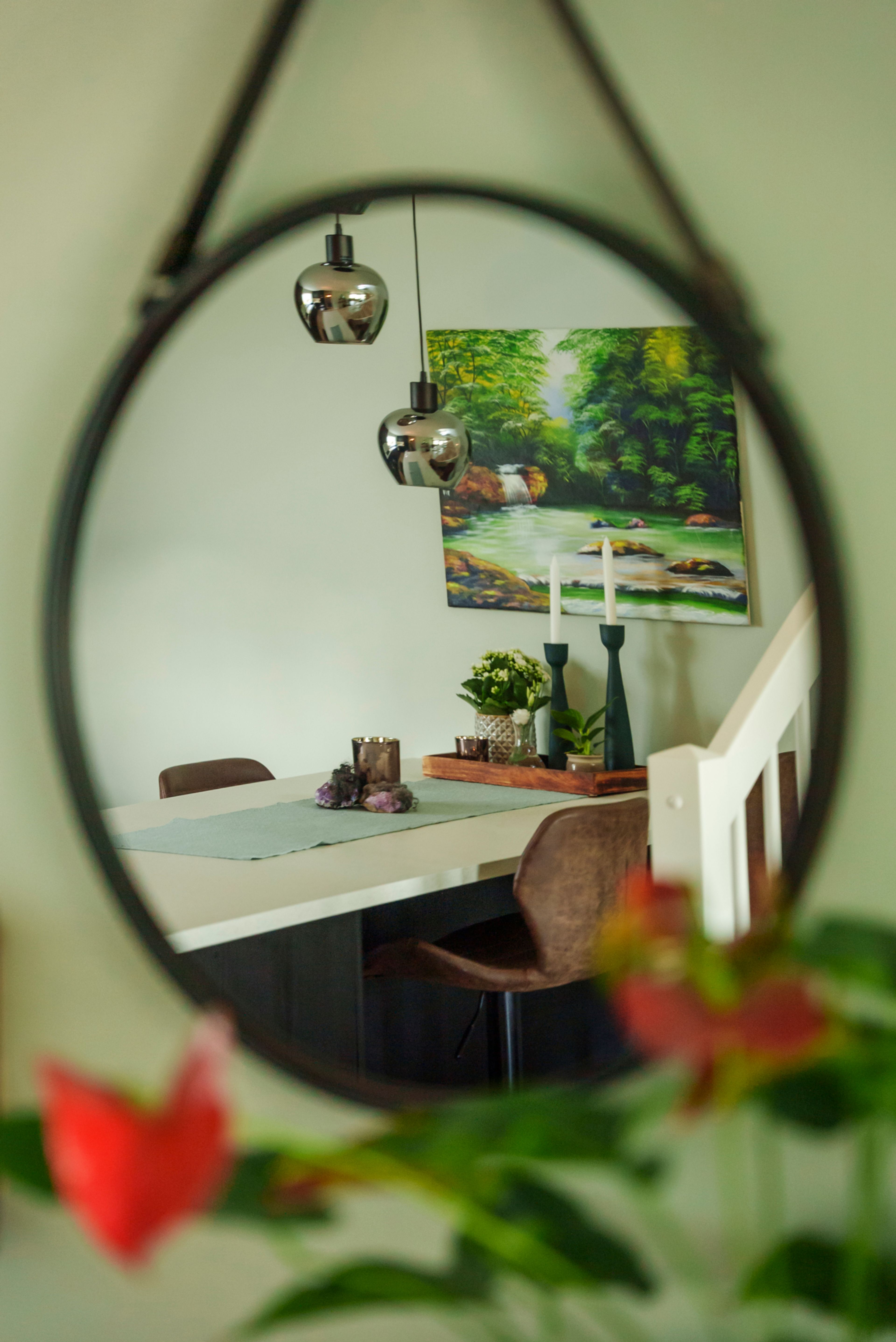 Bilde av et speil som viser et stuebord i bakgrunnen med lys bordplate og mørke stoler. En dus grønnfarge dominerer veggene.