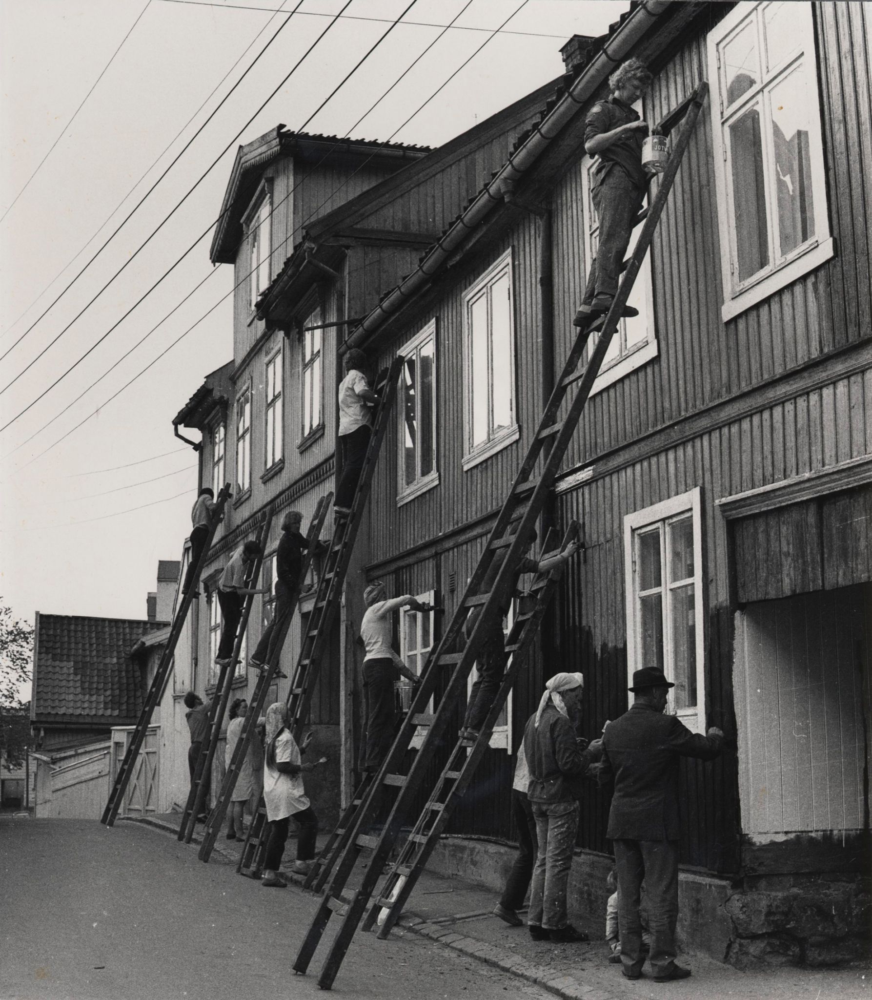 Masse mennesker maler husveggen på dugnad.