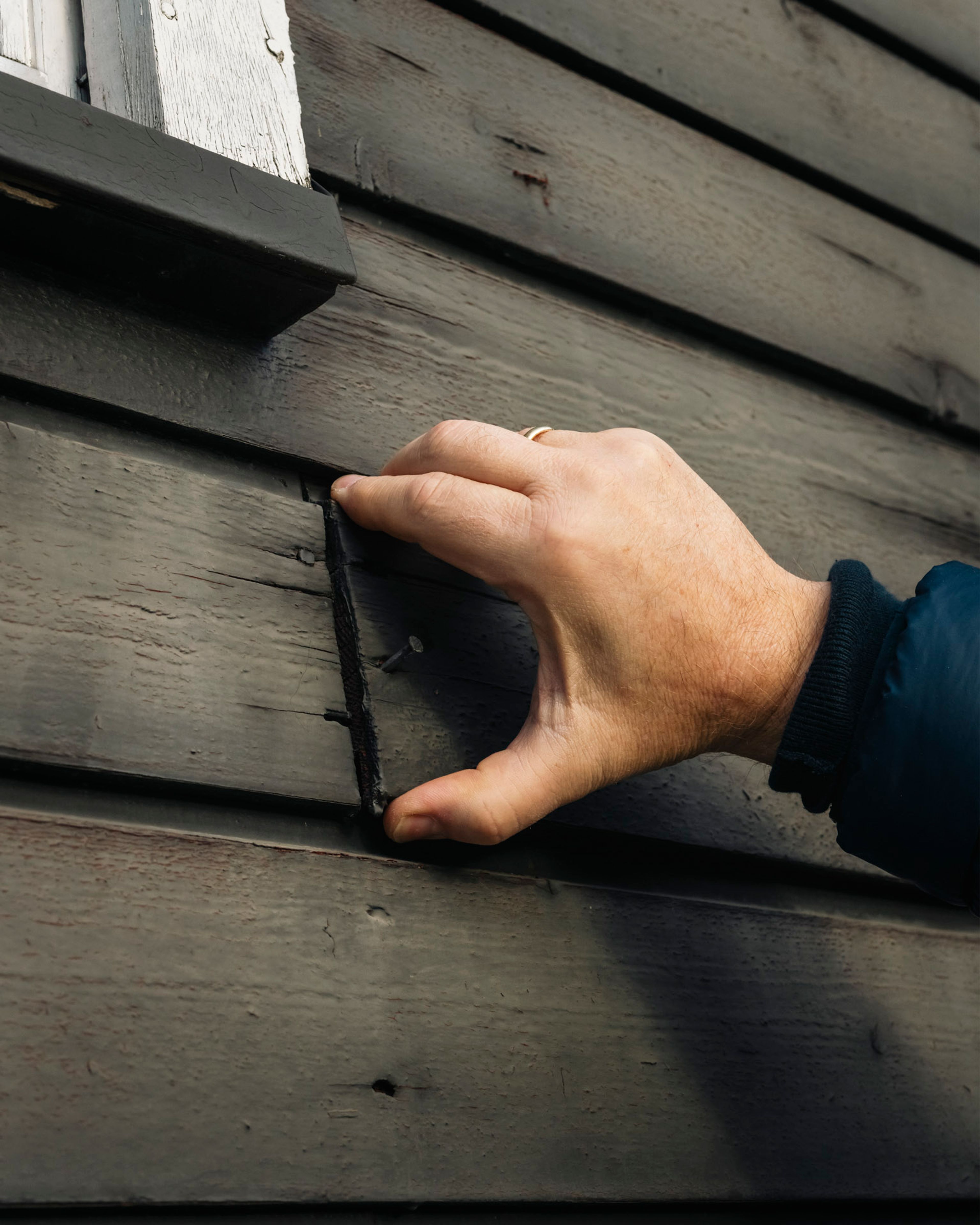 Hånd som peker på slitt trekledning på fritidsbolig, et tydelig tegn på behov for vedlikehold.