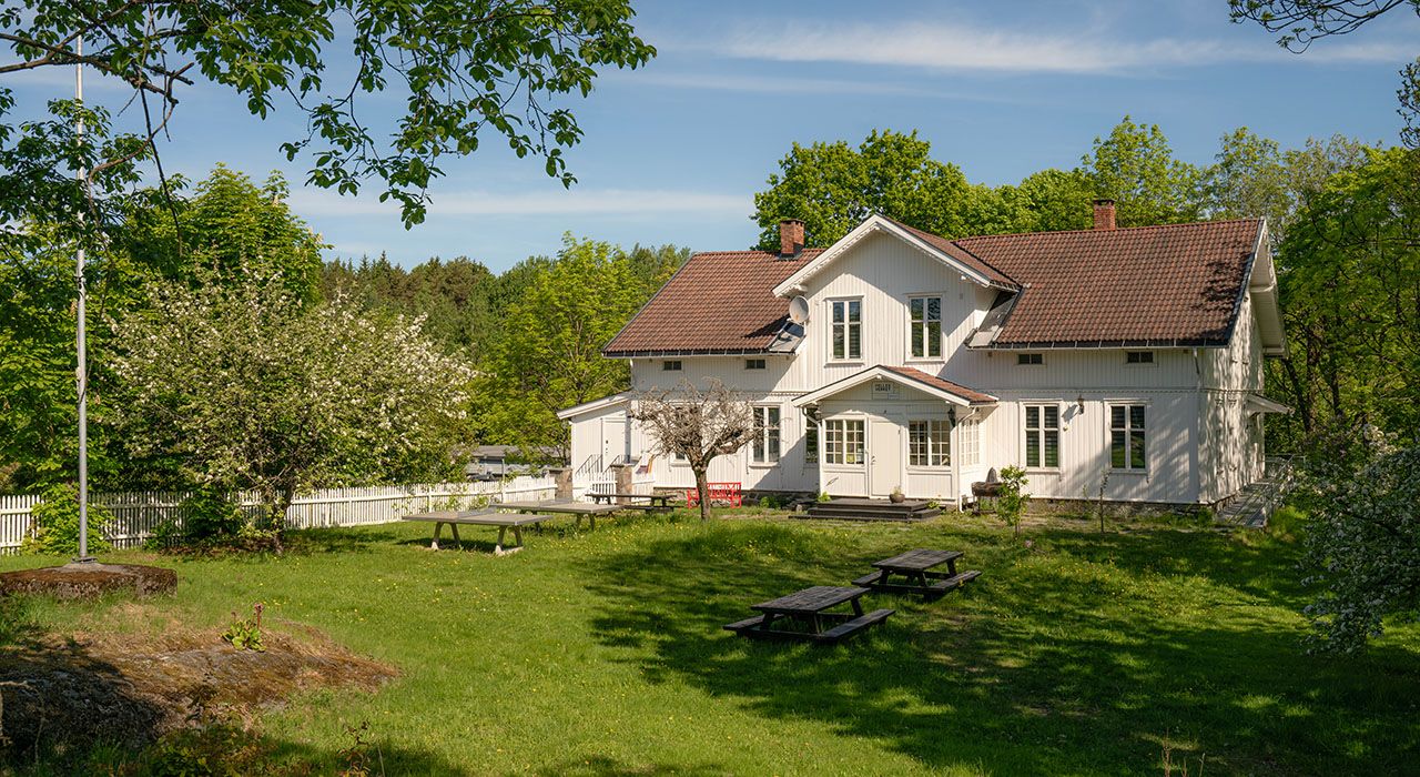 hvitt gammelt hus med en frodig hage.