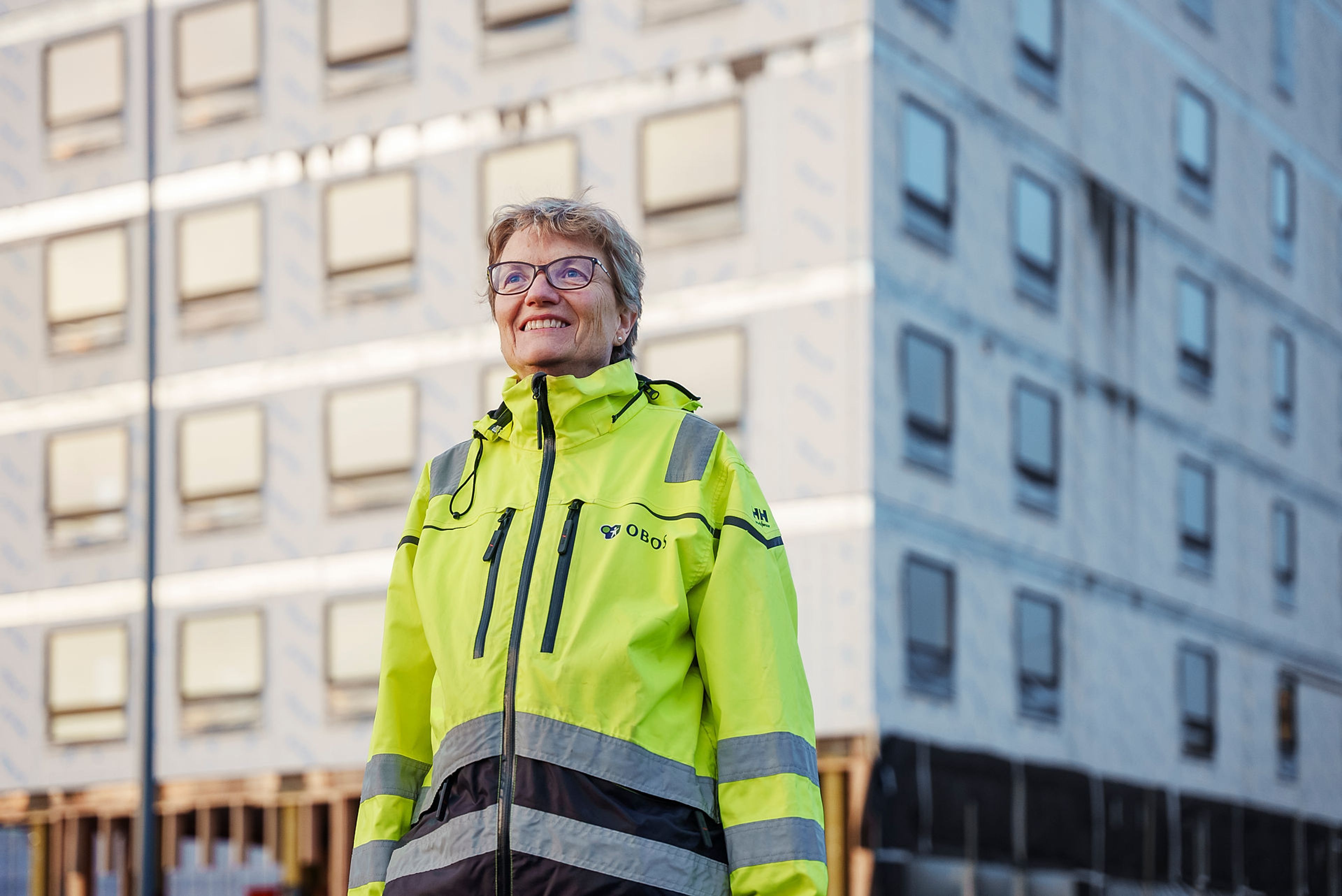 Foto av prosjektleder Wenche Yndesdal som smiler foran byggingen av boligprosjektet Ulvenplassen.