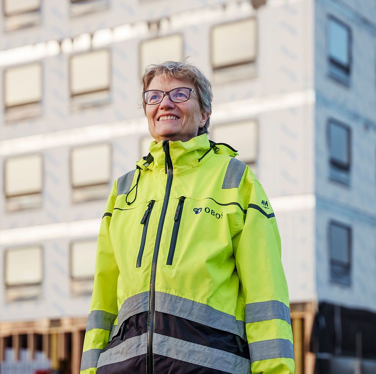 Foto av prosjektleder Wenche Yndesdal som smiler foran byggingen av boligprosjektet Ulvenplassen.