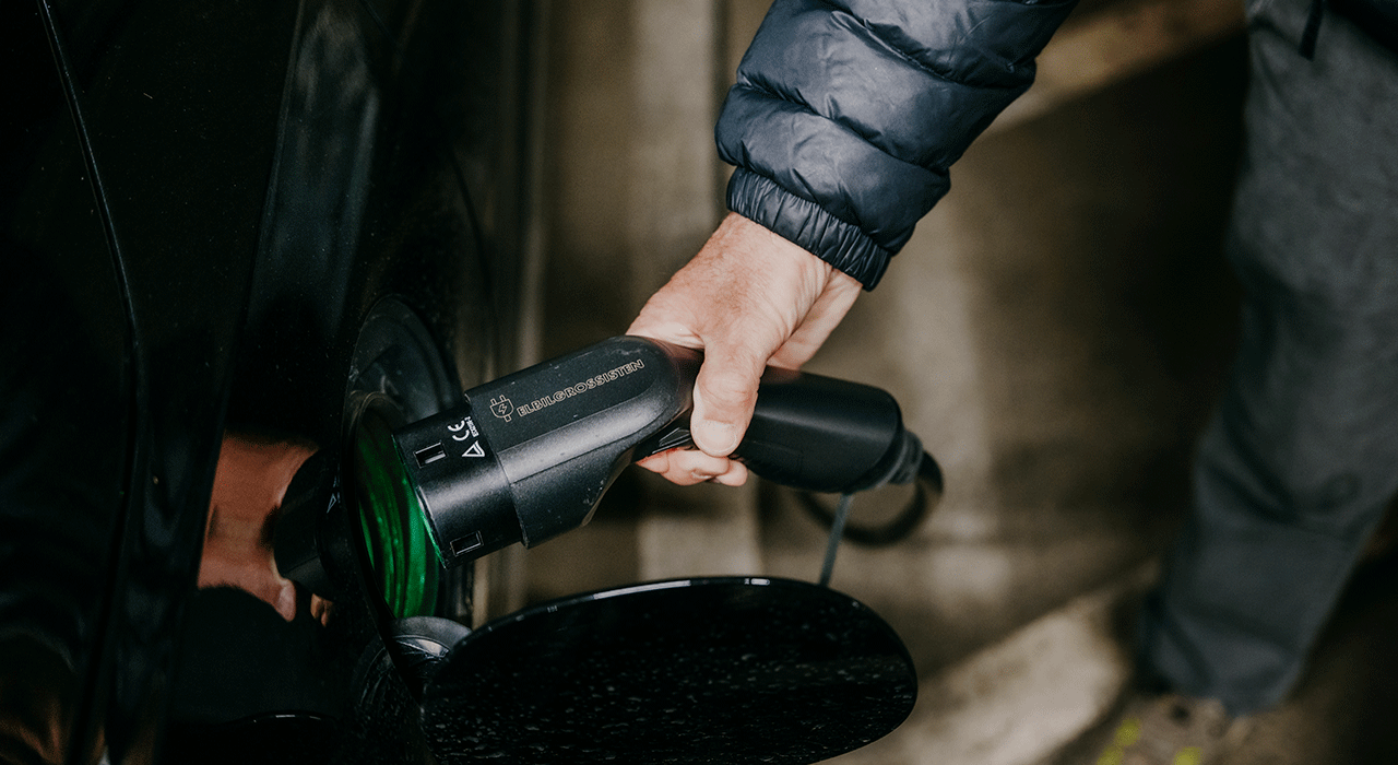 Styreleder Asbjørn Hagerupsen setter en elbillader i ladeporten på en bil.