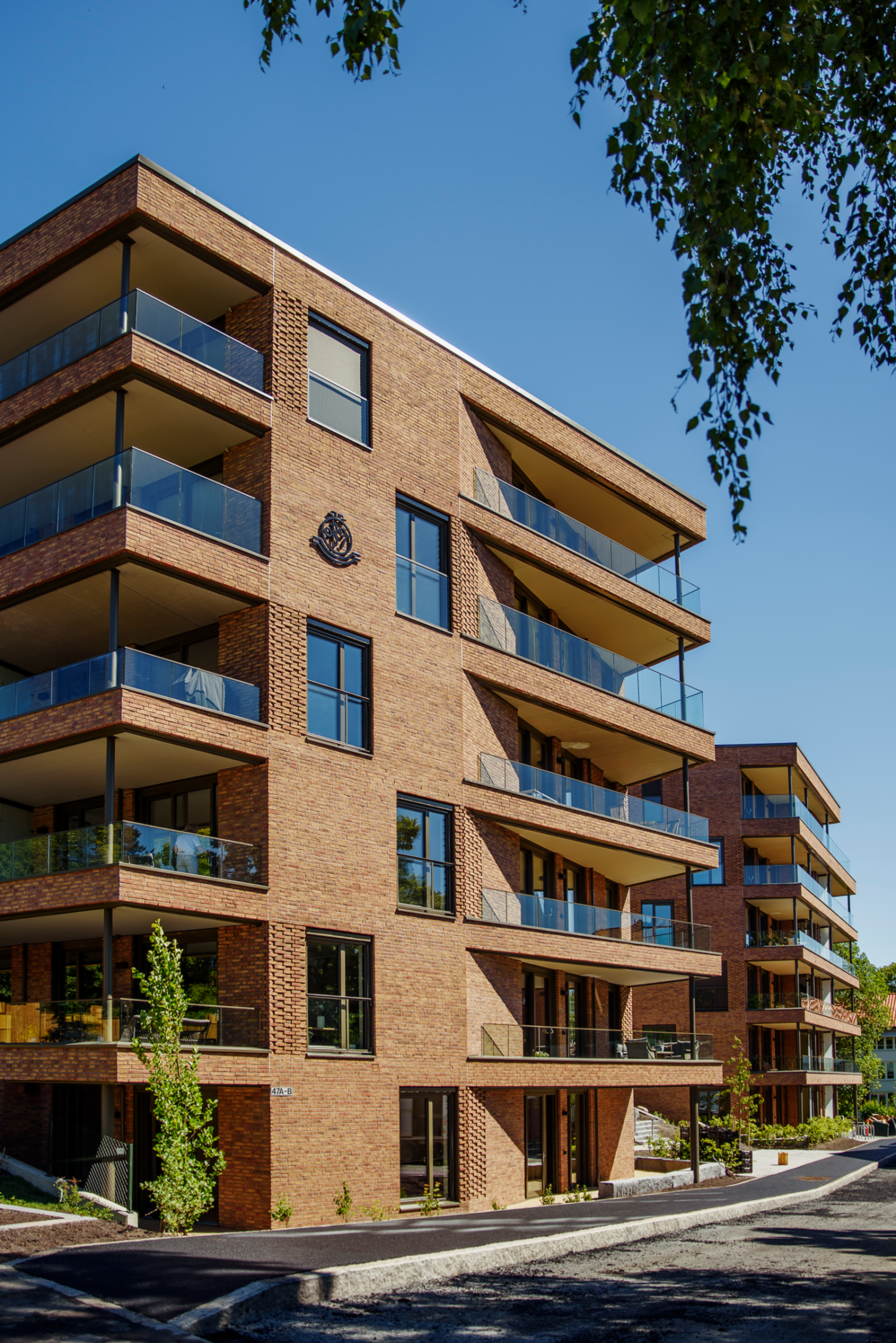 Bilde av fasaden til en av blokkene i Hoffsveien Hage som bader i solen. Brun teglstein og glass går igjen.