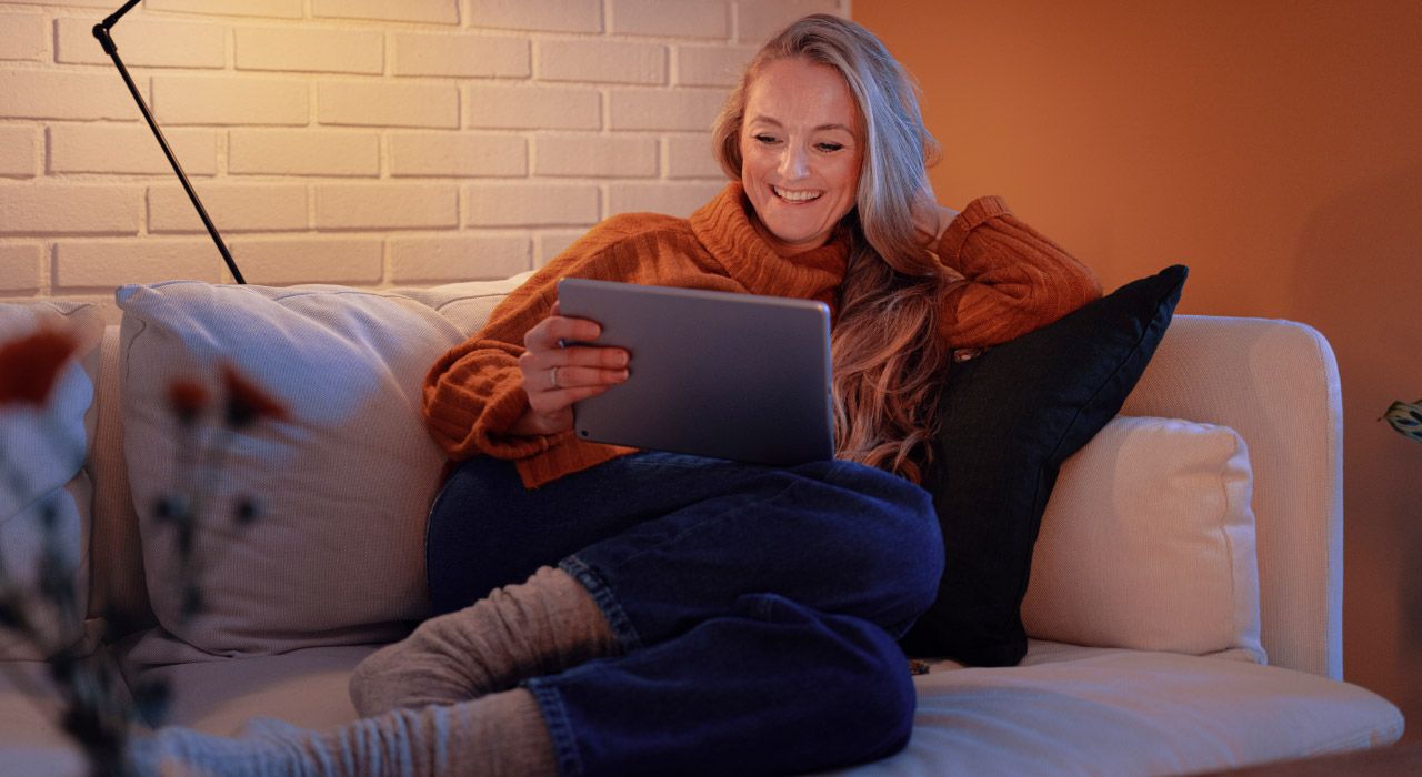 Kvinne sitter i en sofa og ser på en pad