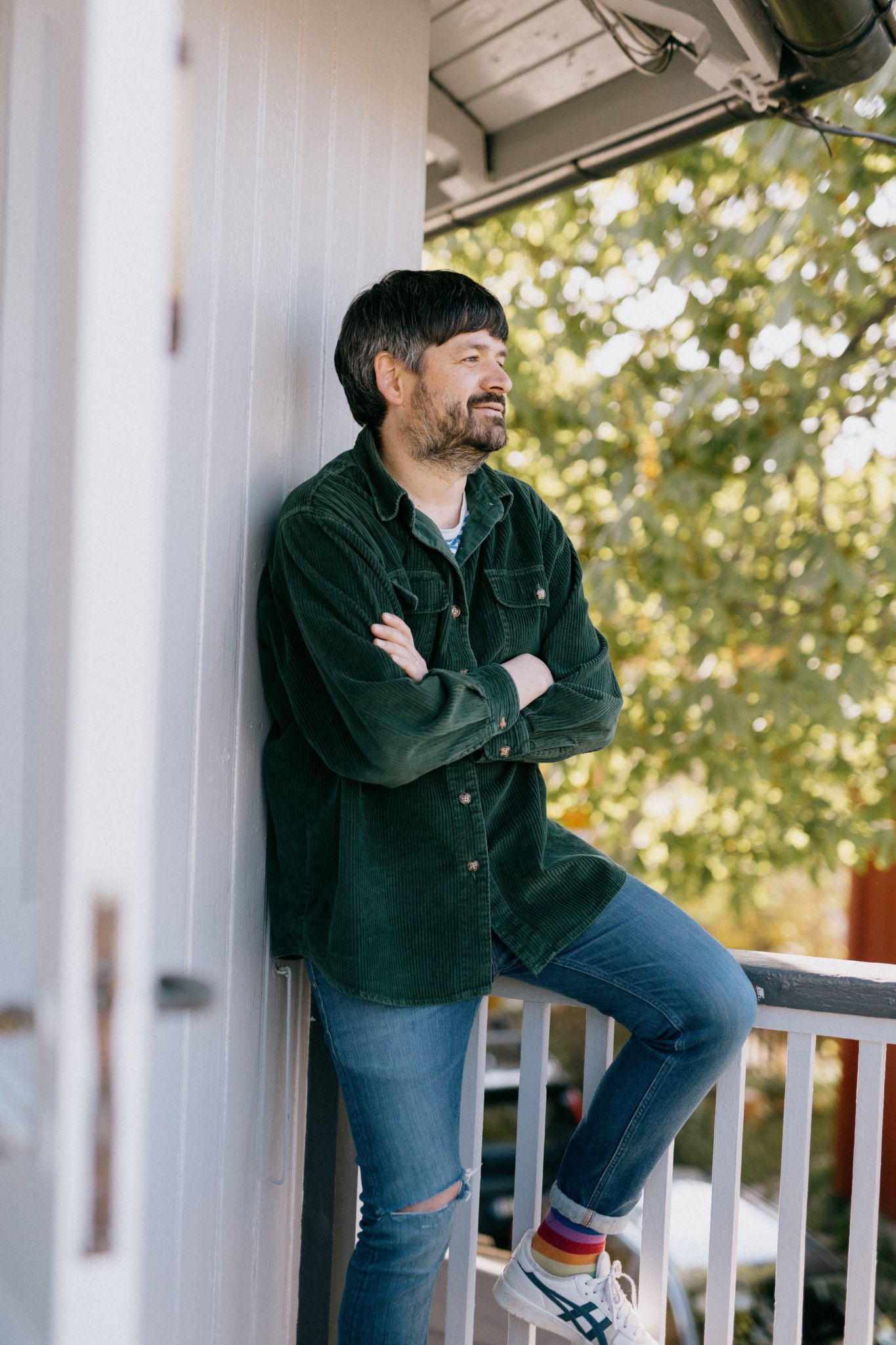 Mann har armene i kors og lener seg mot en hvit vegg. Han smiler.