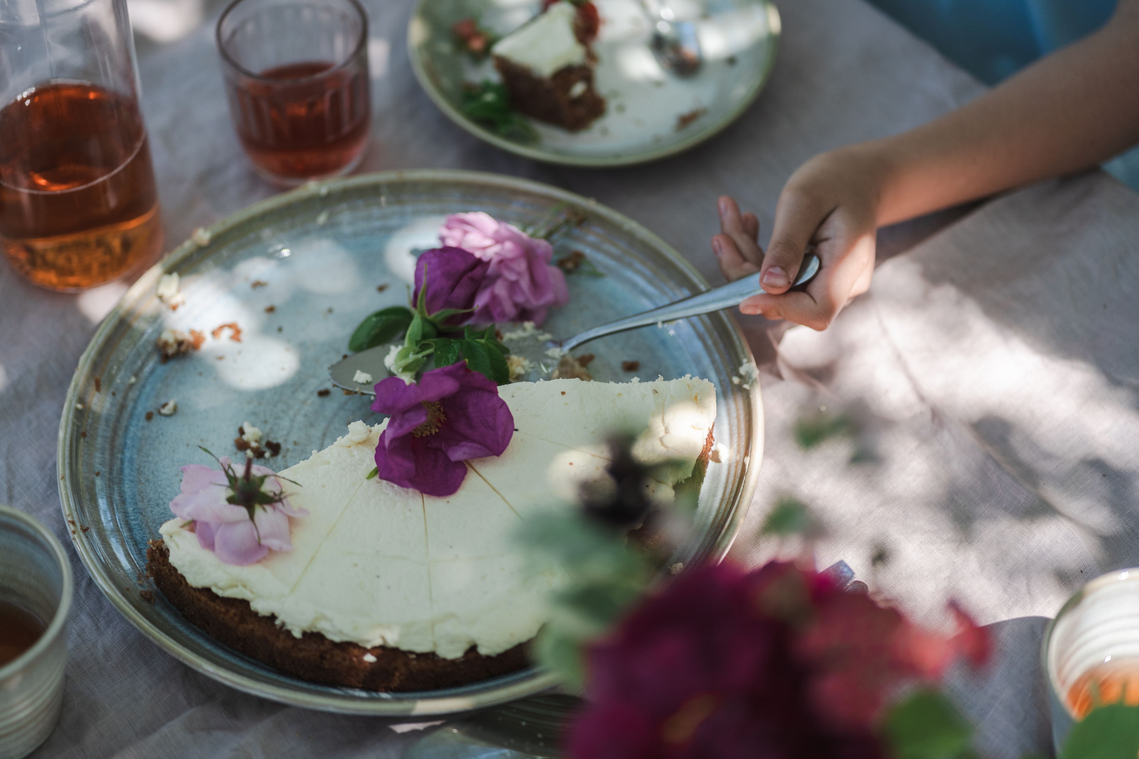 Somrig bild med en tårta med blomsterdekoration, på ett bord med linneduk