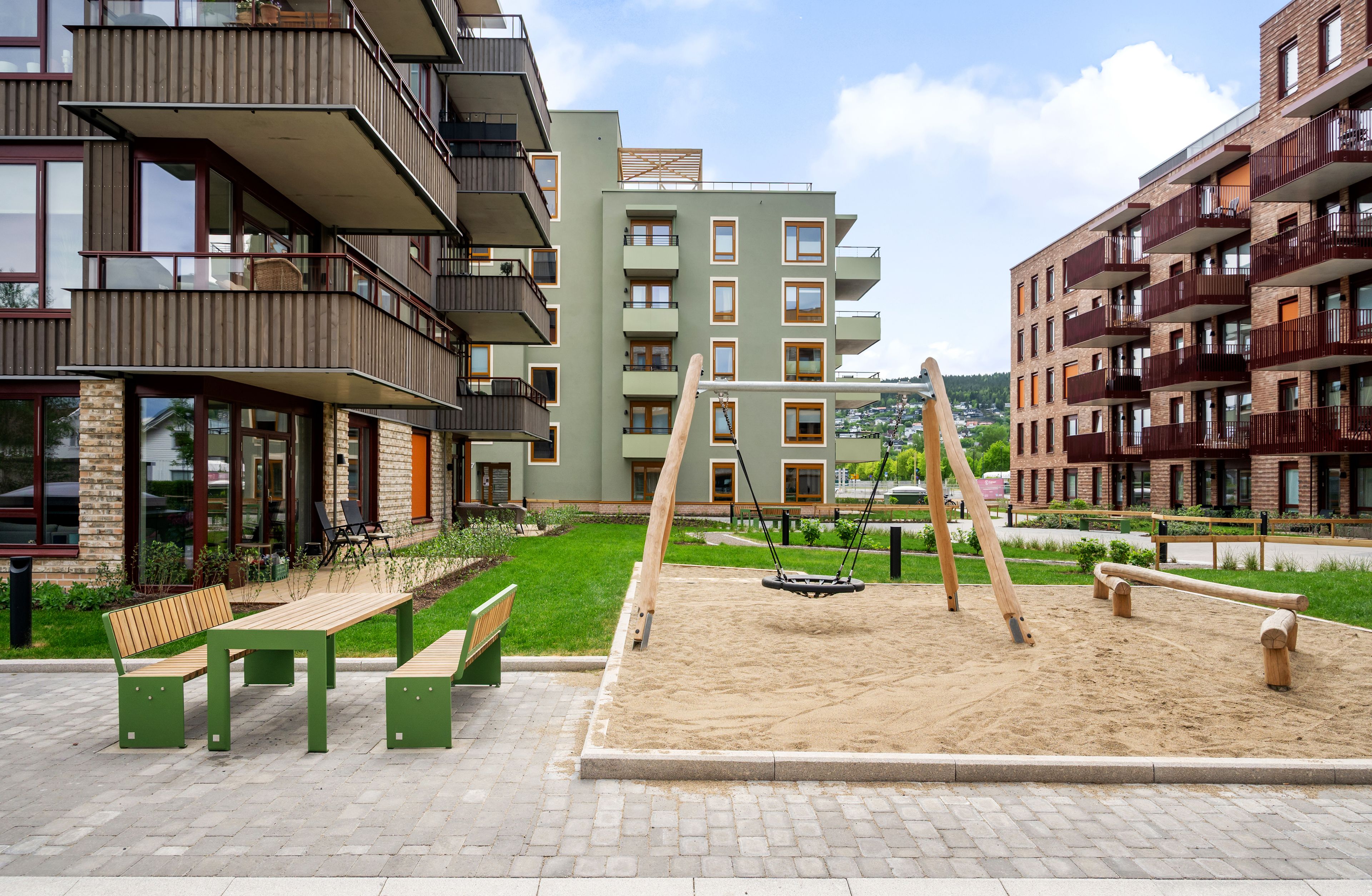 foto av uteområde med benker, bord og lekeplass med huske og sandkasse