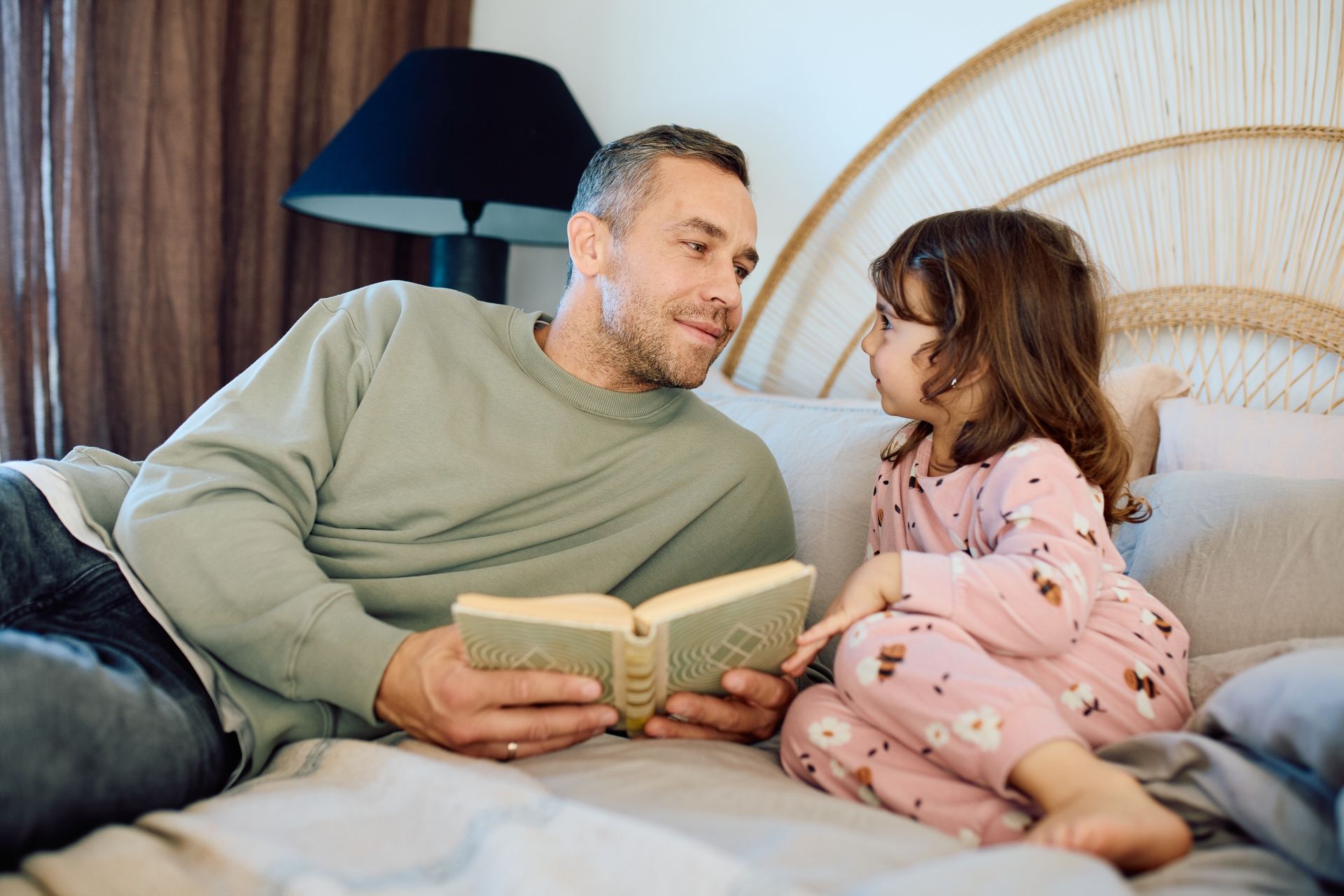 Foto av far og datter som leser bok på sengen