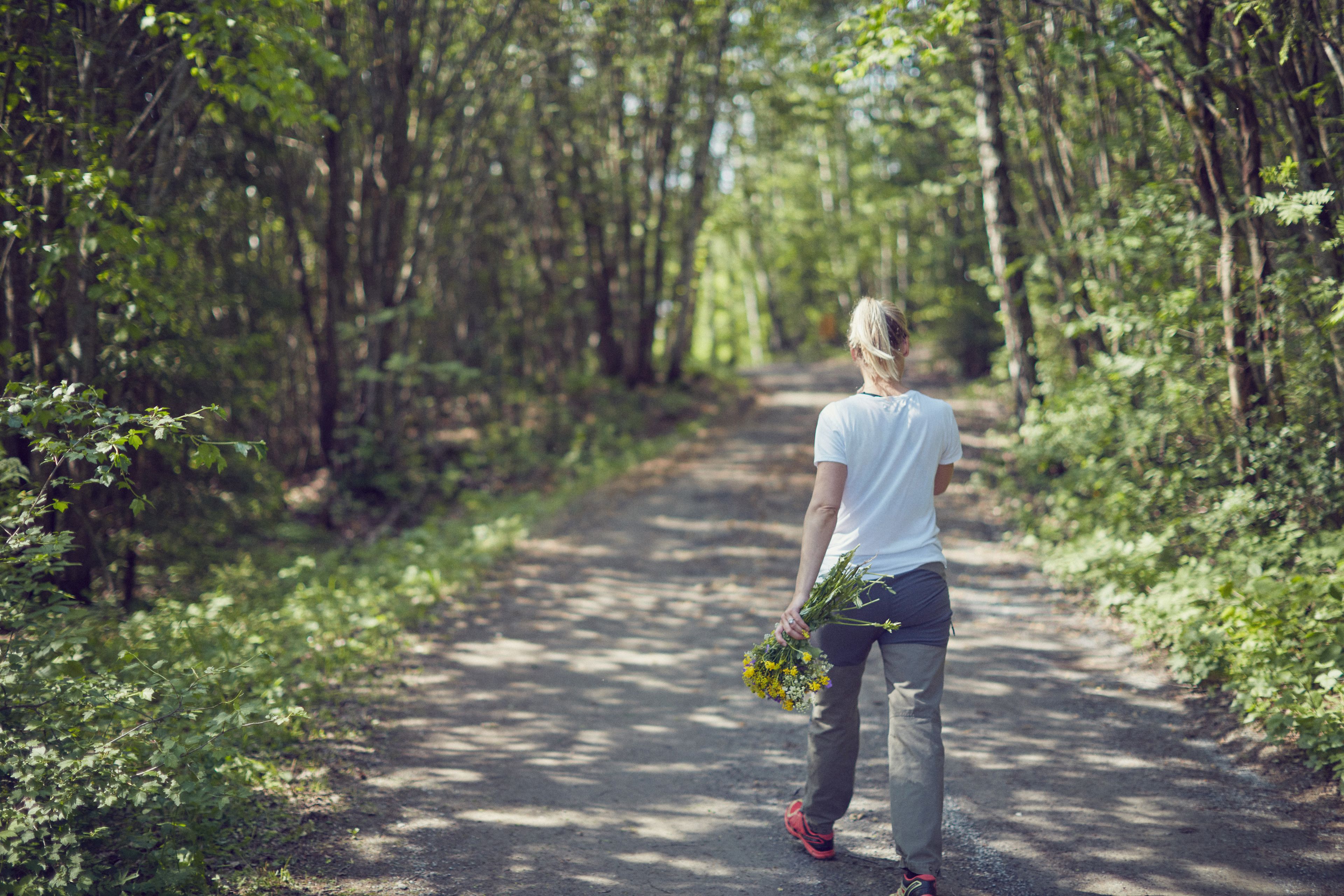 Dame går tur på grusvei i skogen med en blomsterbukett i hånden