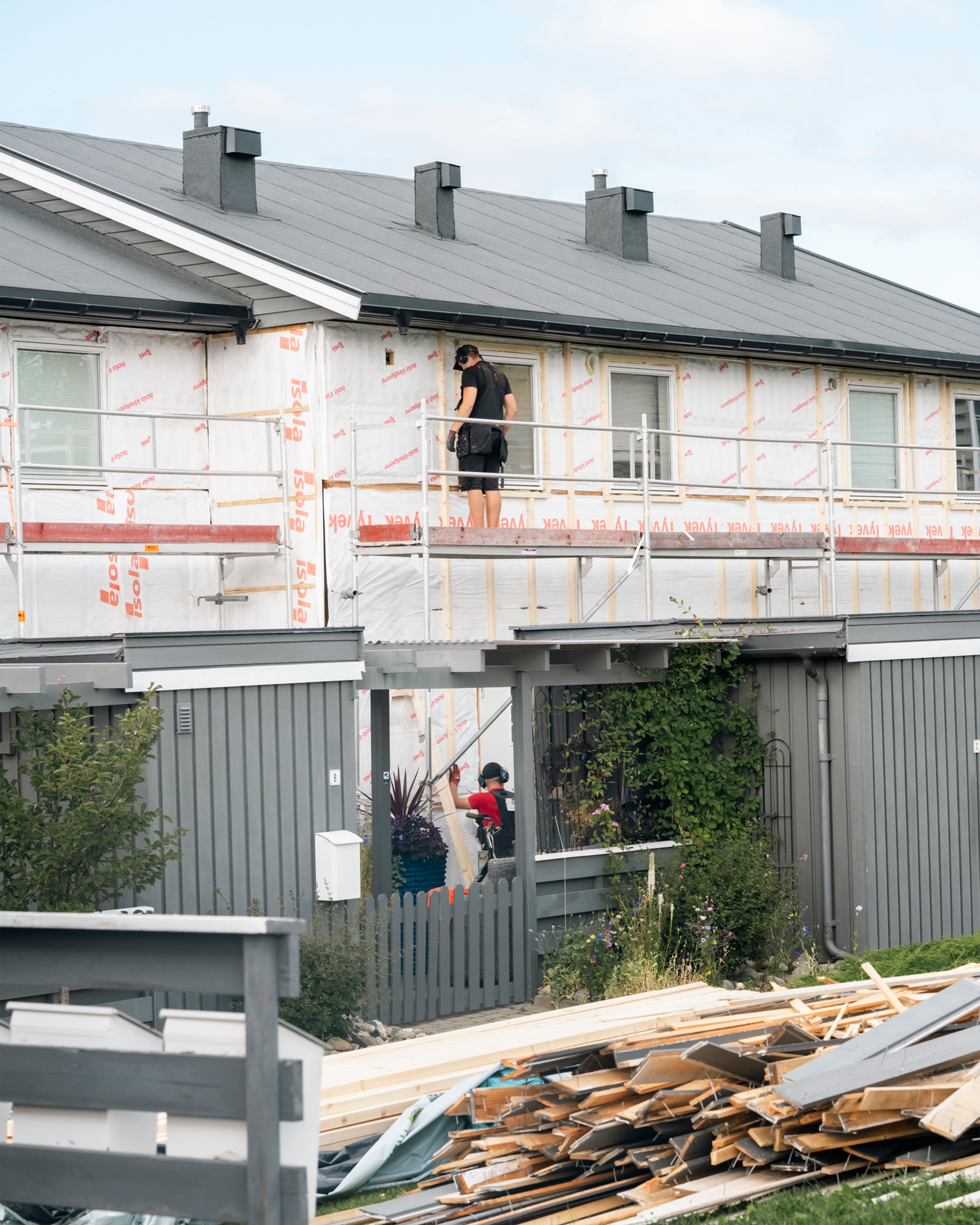 Rekkehus under rehabilitering med arbeidere på stillas og avdekket fasade.