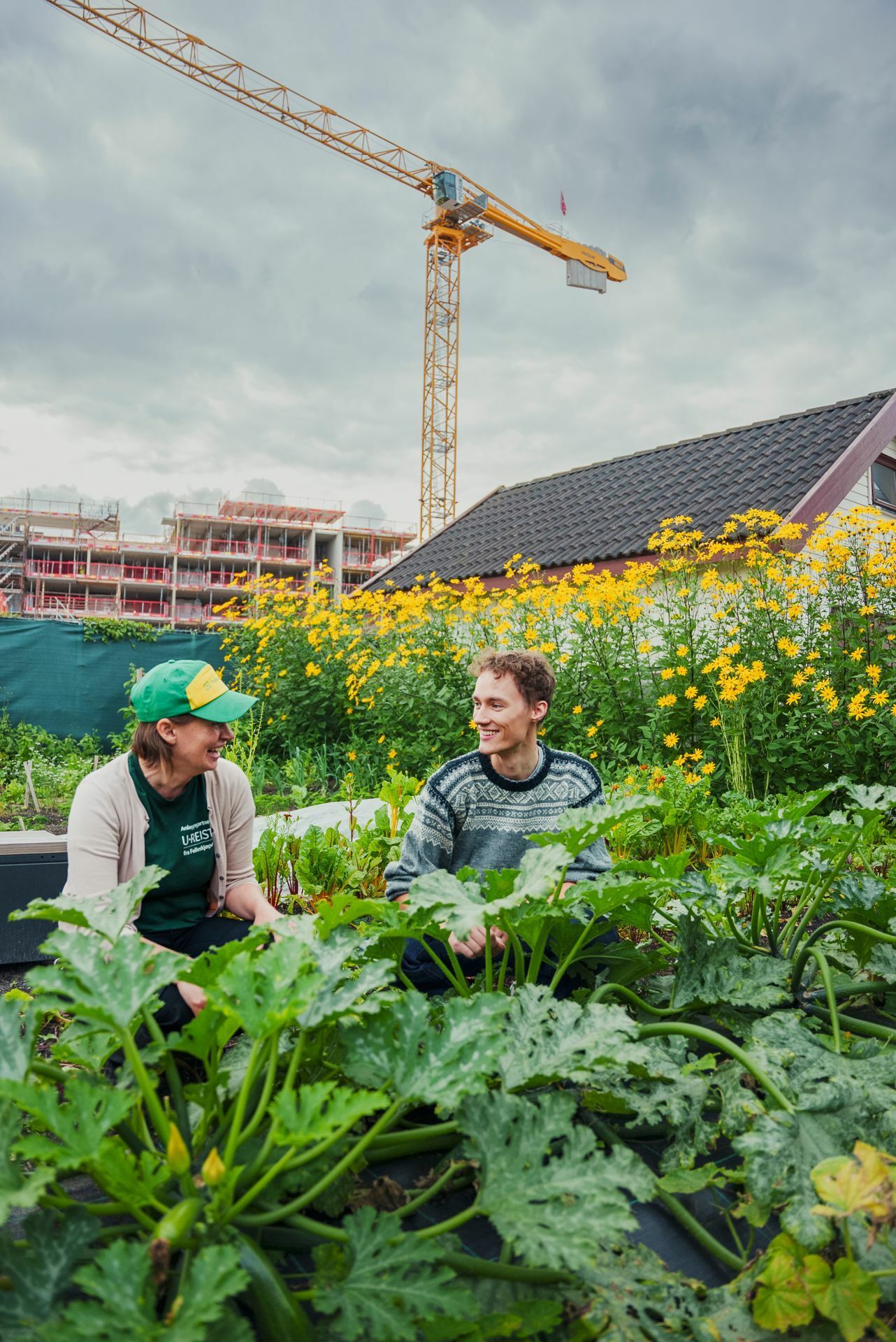 Sigurd og en av naboene, en dame med grønn caps og grønn t-skjorte, sitter sammen i beddet og snakker sammen.