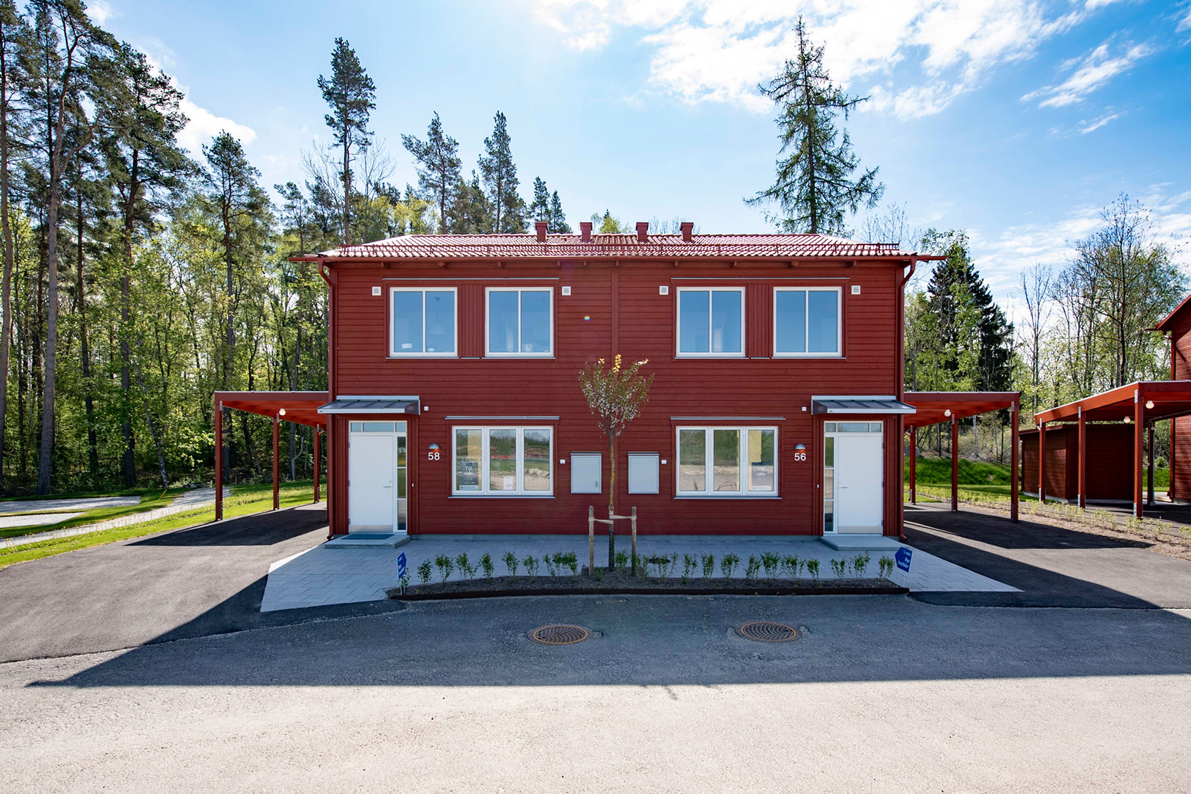 Exteriör rött parhus med vita ytterdörrar och carport