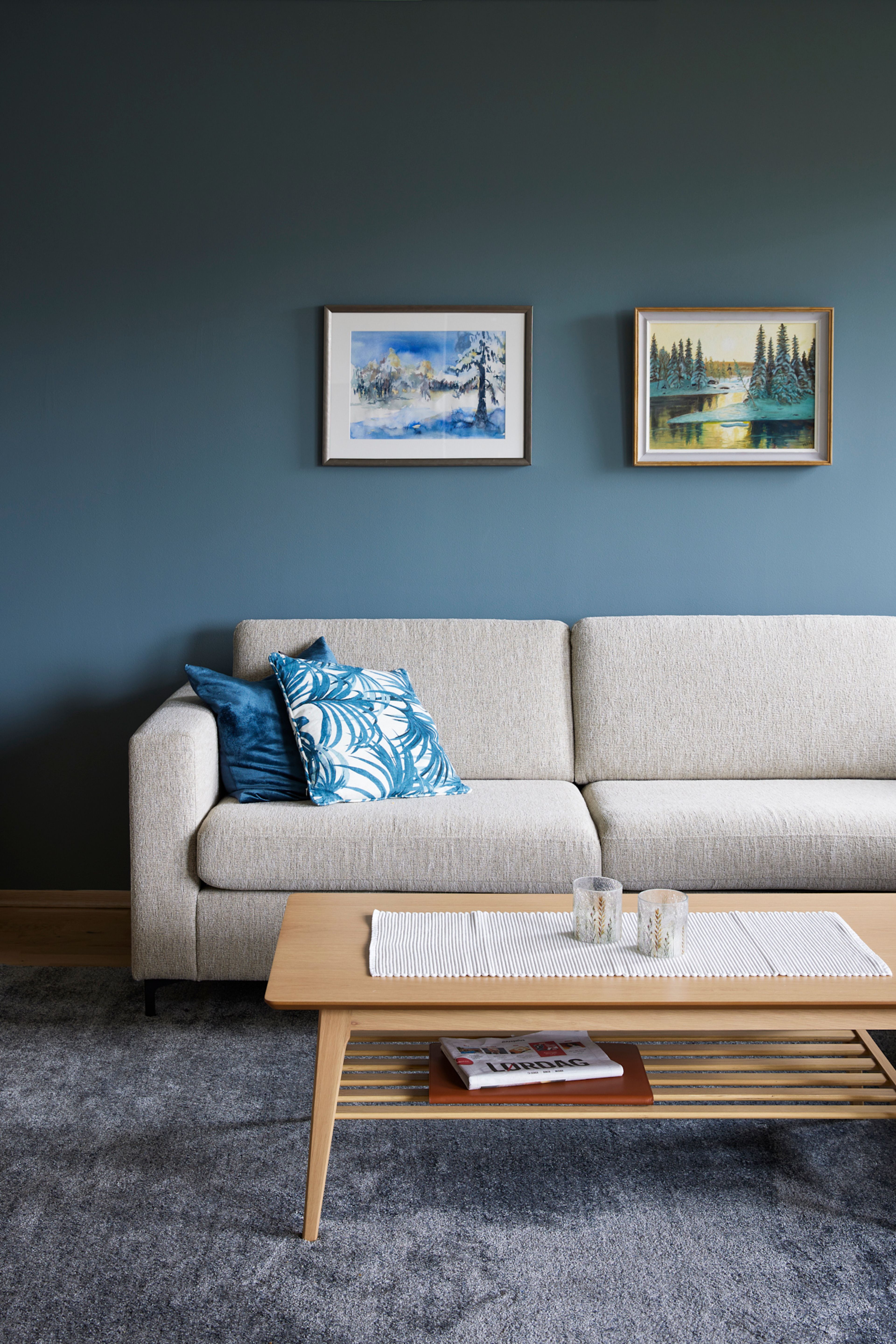 Beige sofa og trefarget stuebord foran en blåmalt stuevegg.