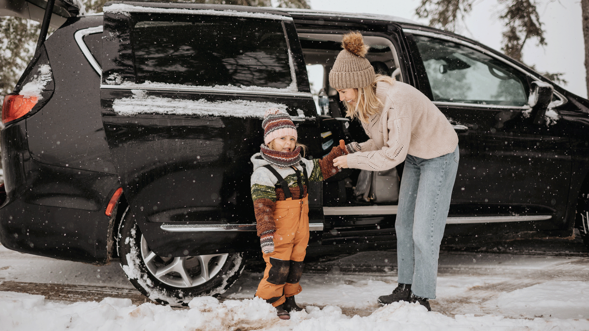 Kvinna som sätter på sitt barn en vante vid en bil.