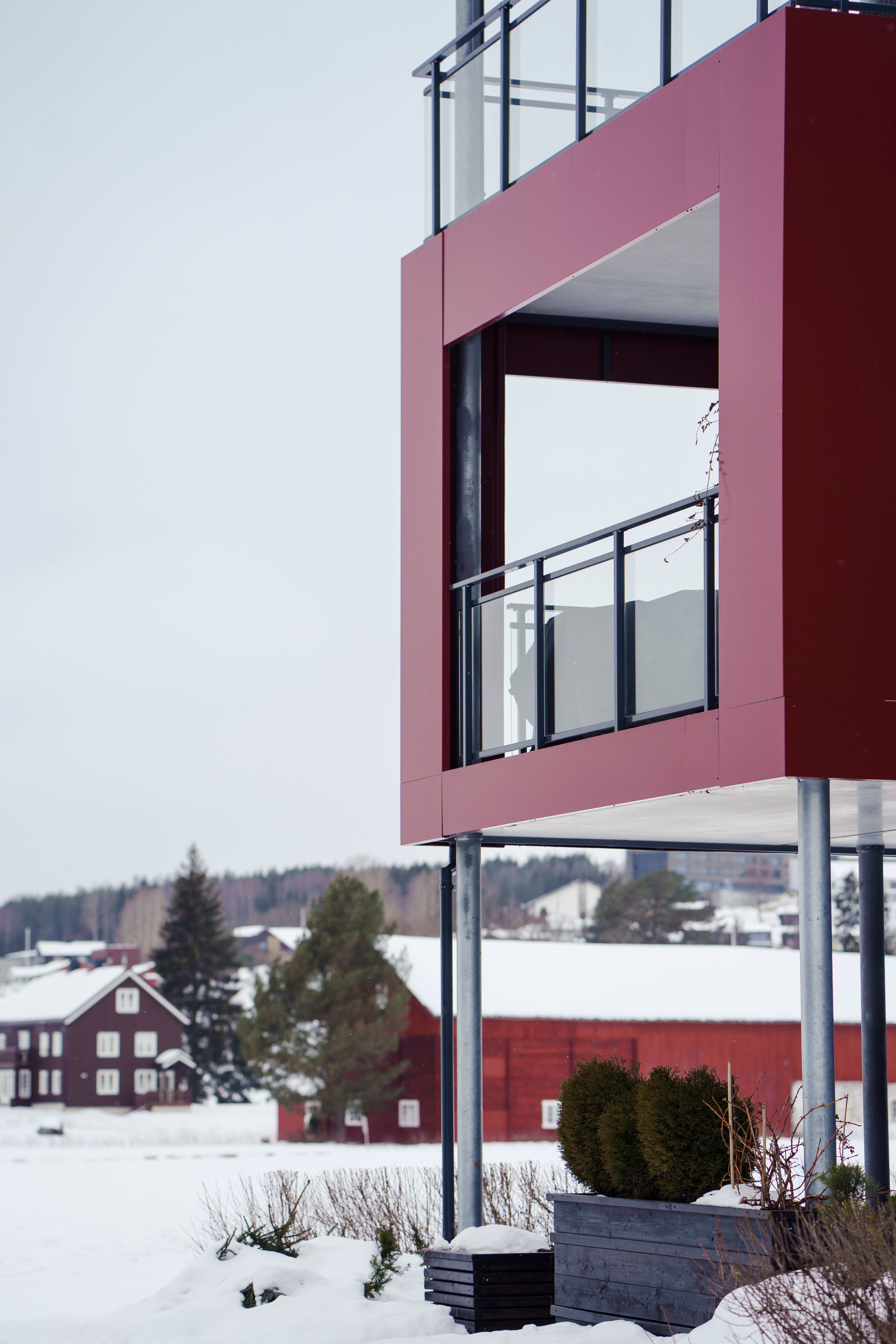Bilde som viser en hjørneleilighet med balkong mot en bakgrunn av snø og røde gårdsbygg