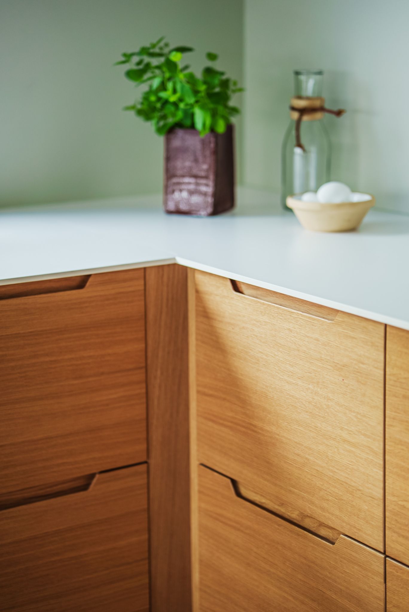 Detaljer av kjøkkeninnredning i tre og hvit benkeplate, med noen kjøkkenartikler stående på benken.