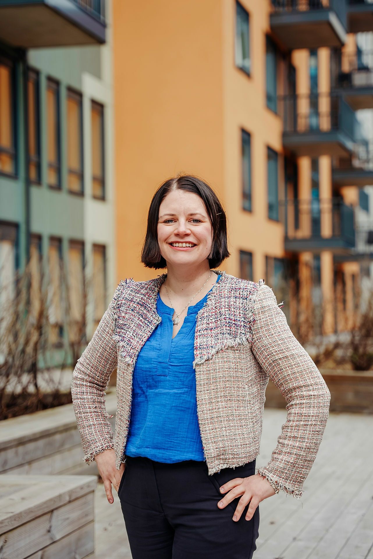 Bilde av en kvinne med kort brunt hår som står foran noen leiligheter med grønn og gul fasade.