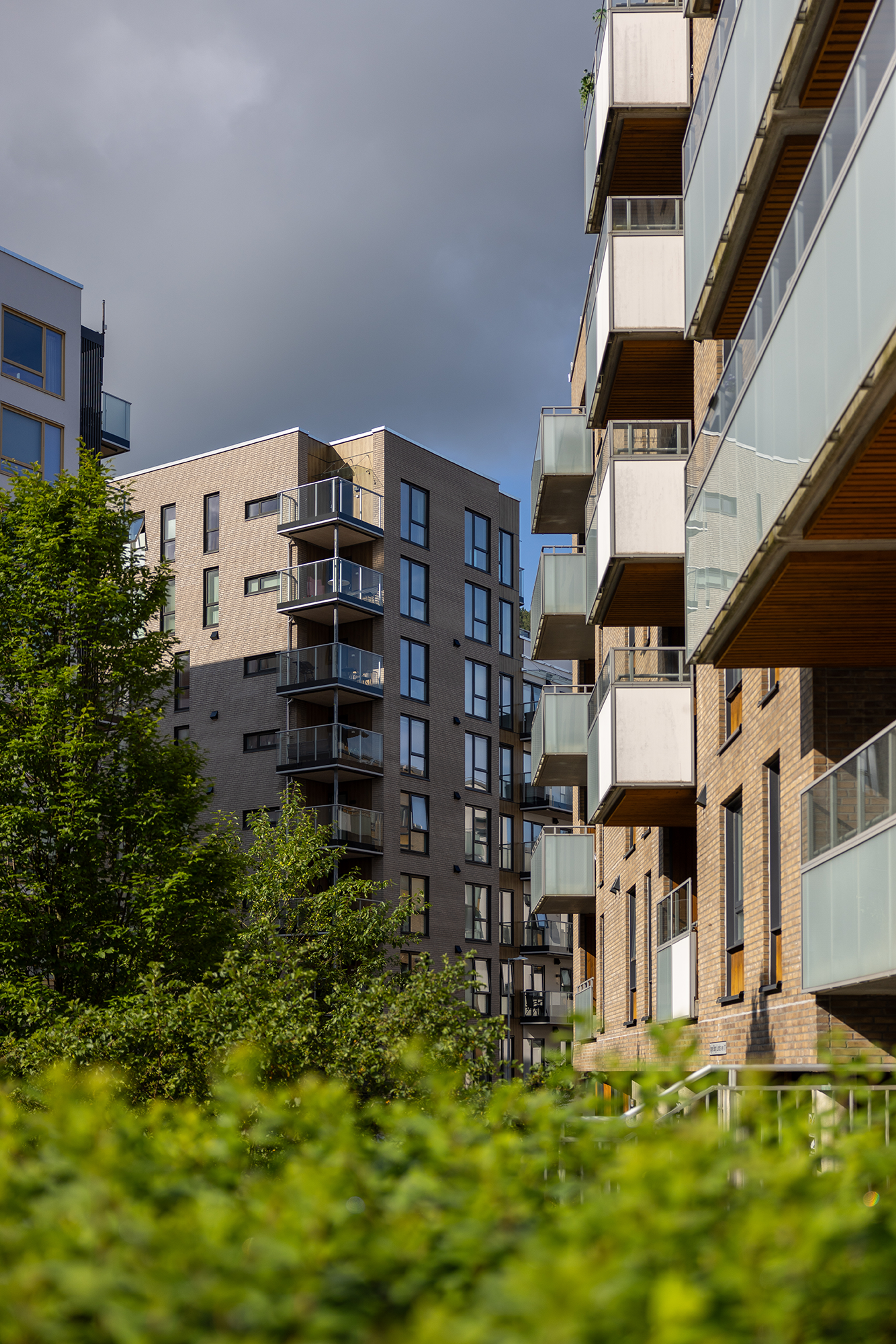 Bilde av fasaden til to ulike bygg i Kronstadparken, begge i brun farge med grå balkonger. Foran i bildet er det grønne busker.